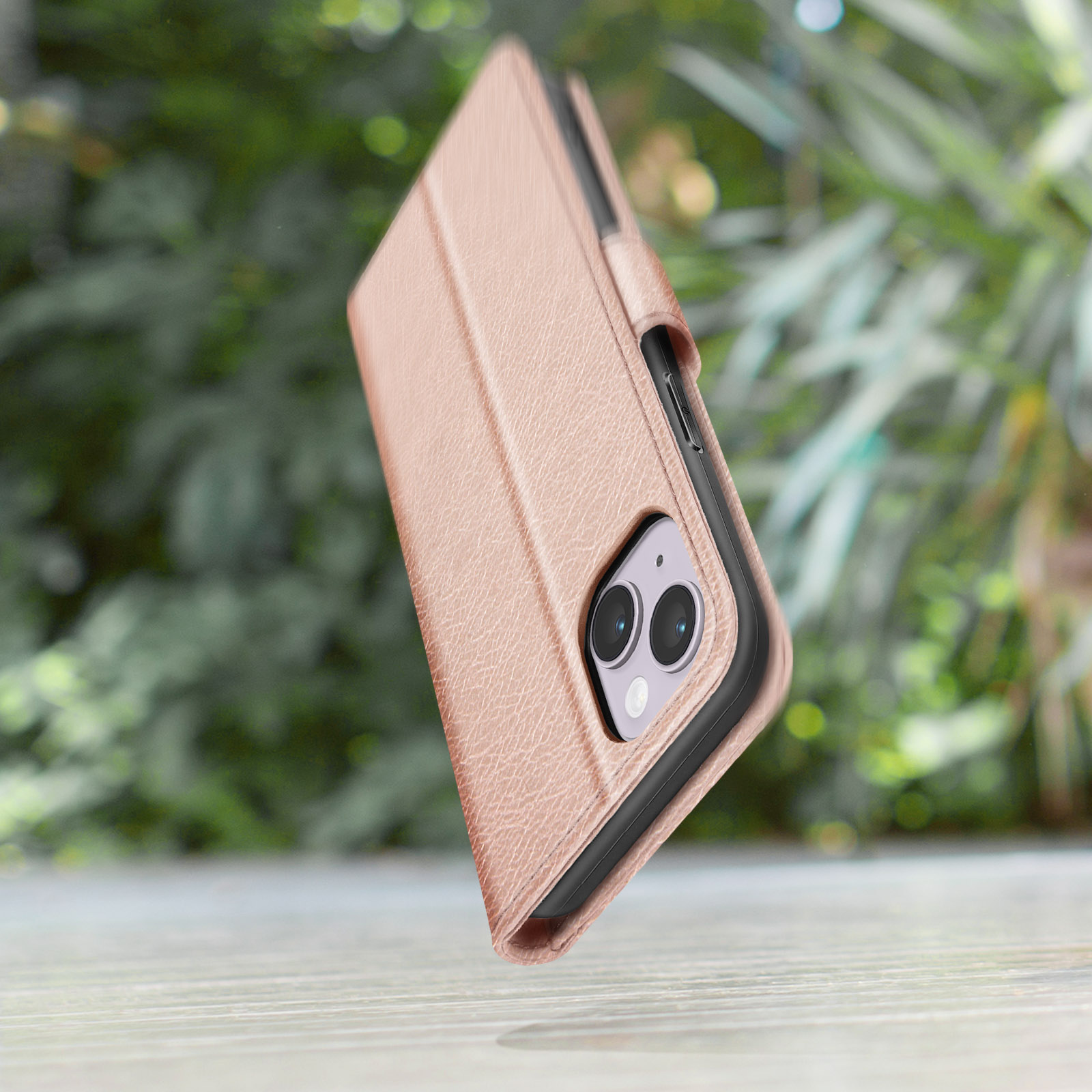 Una cover per telefono testurizzata oro rosa su un tavolo di legno. Sfondo di fogliame verde.