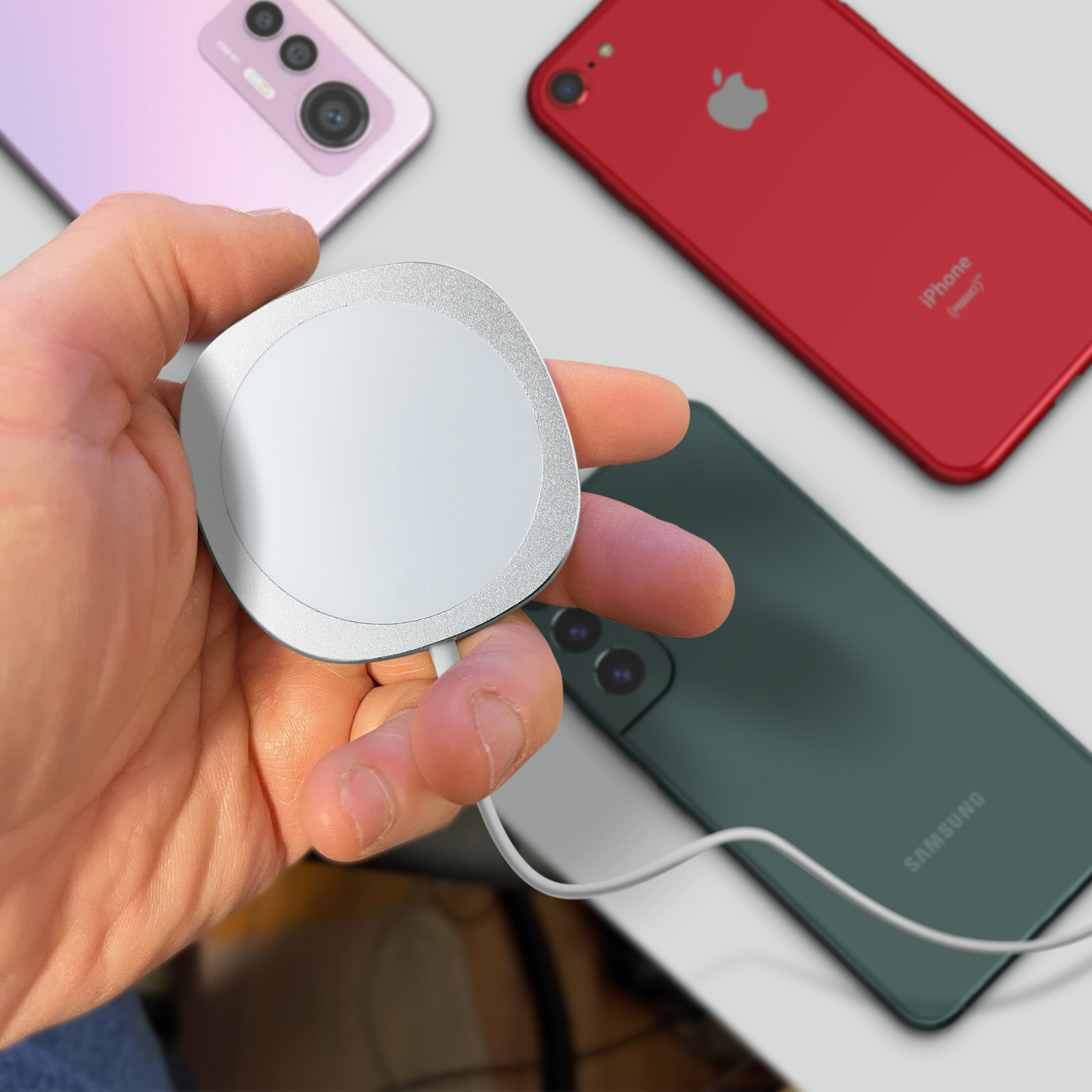 Una mano tiene un caricatore magnetico bianco vicino a uno smartphone rosa, rosso e verde.