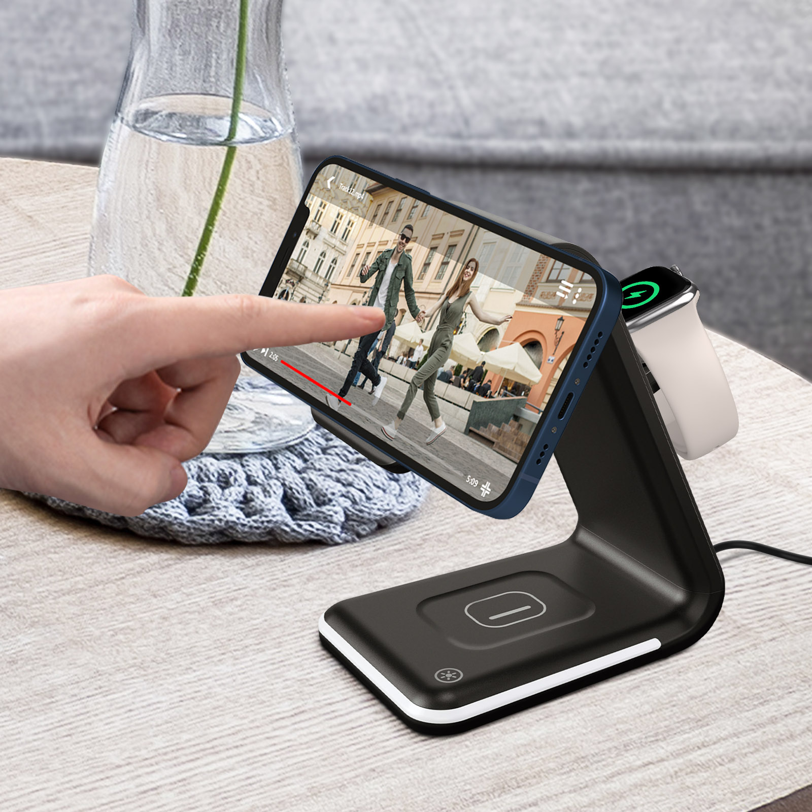 Ein Smartphone und eine Smartwatch laden auf einem schwarzen Ständer, daneben eine Vase.
