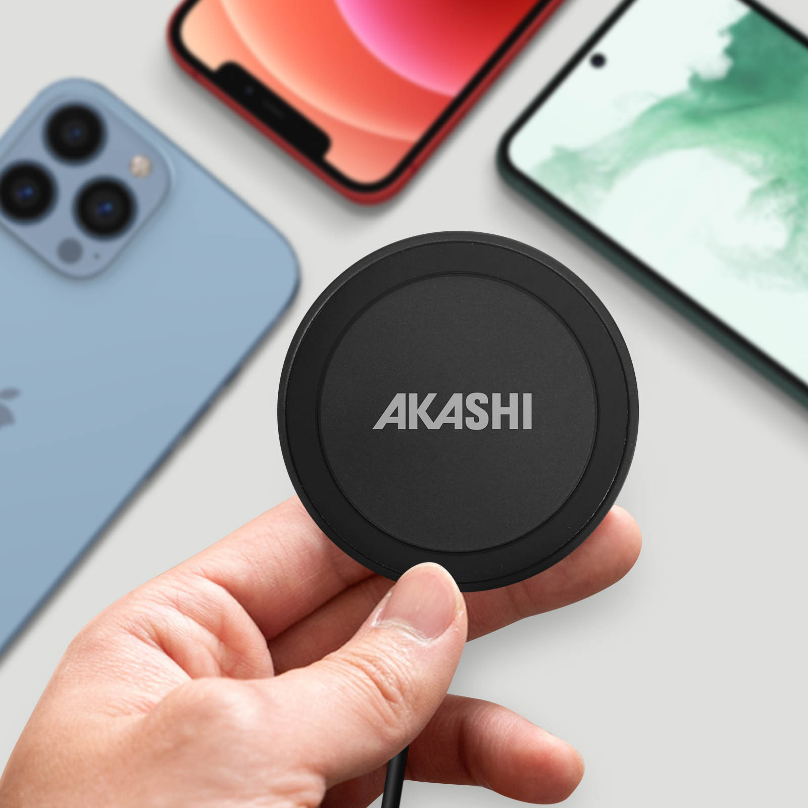 Eine Hand hält ein schwarzes Akashi Ladegerät vor drei Smartphones.