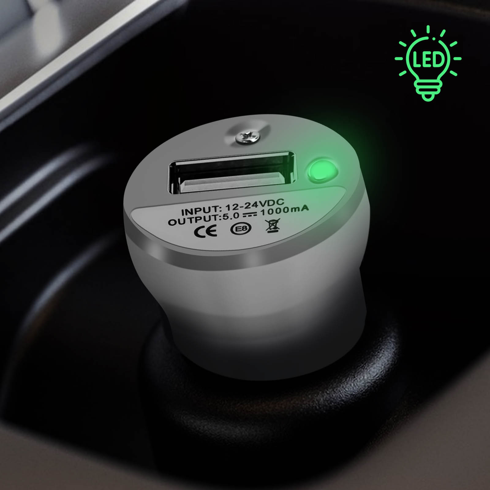 Adattatore auto USB grigio con LED verde in un portabicchieri scuro.