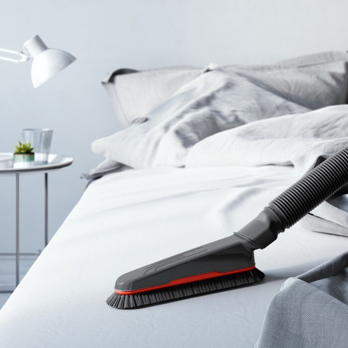 Una spazzola per aspirapolvere giace su un letto bianco.