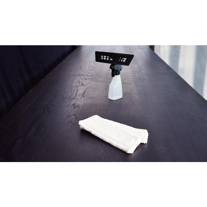 Un panno mocio bianco e una bottiglia spray su un tavolo di legno scuro.