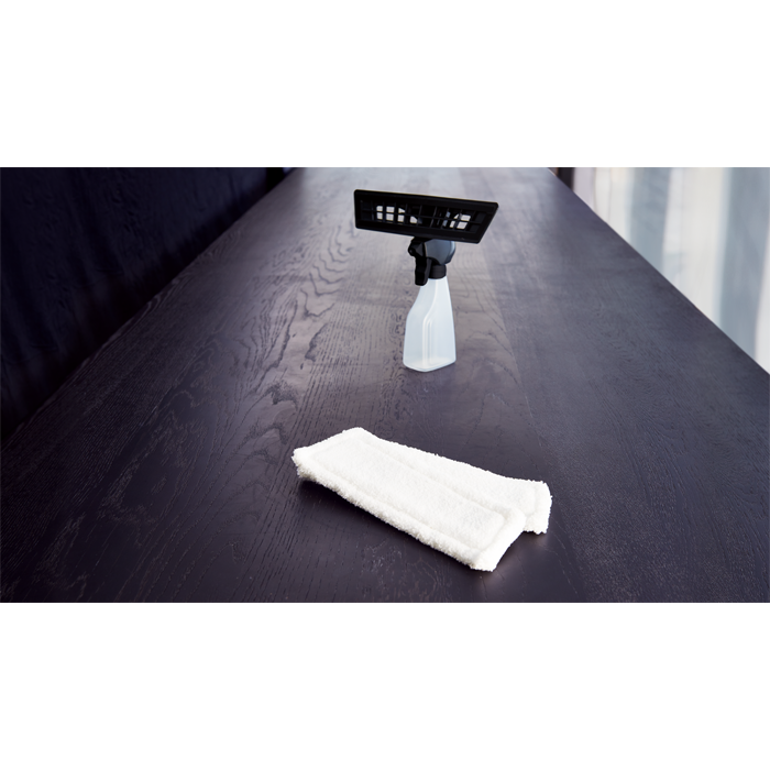 Una testa di mop bianca e una bottiglia spray con attacco nero su un tavolo di legno scuro.
