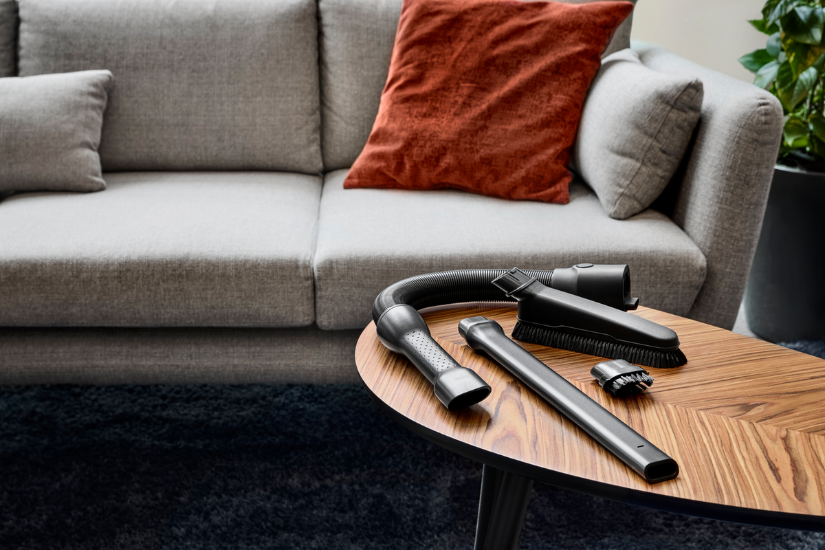 Divano grigio, cuscino, tavolo in legno con accessori e tubo aspirapolvere.