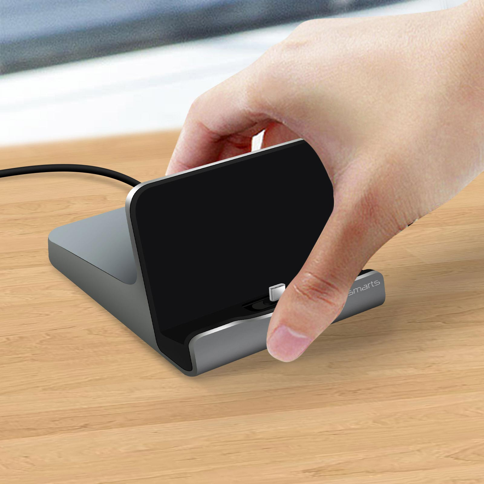 Una mano posiziona uno smartphone su una base di ricarica grigia con schermo nero.
