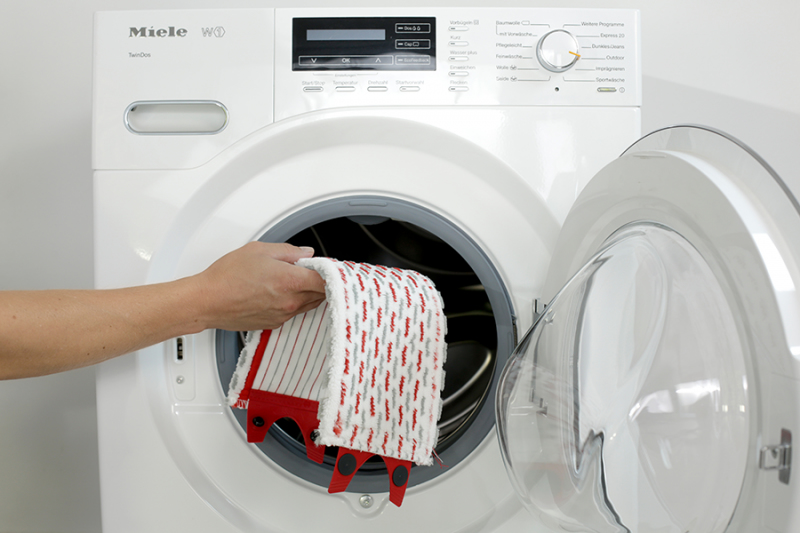 Una mano inserisce uno straccio rosso e bianco in una lavatrice Miele bianca.