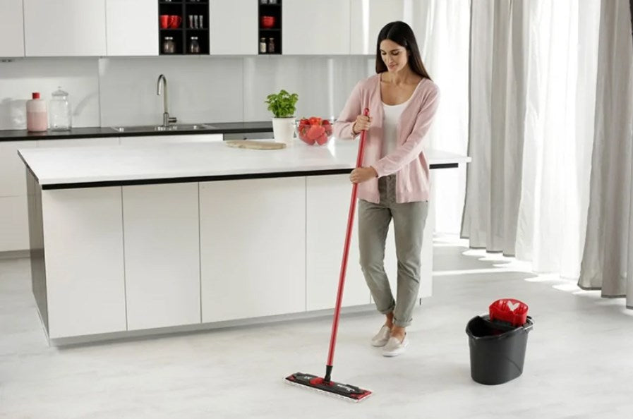 Una donna con uno straccio pulisce il pavimento in una cucina moderna.
