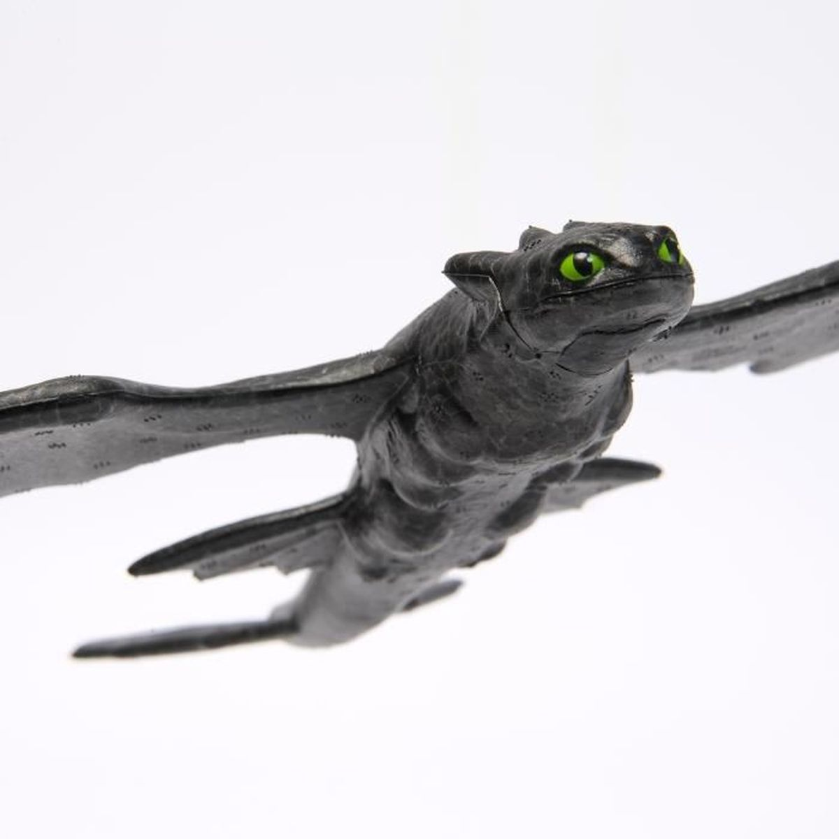 Un juguete de dragón negro con ojos verde brillante, alas extendidas, sobre fondo blanco.