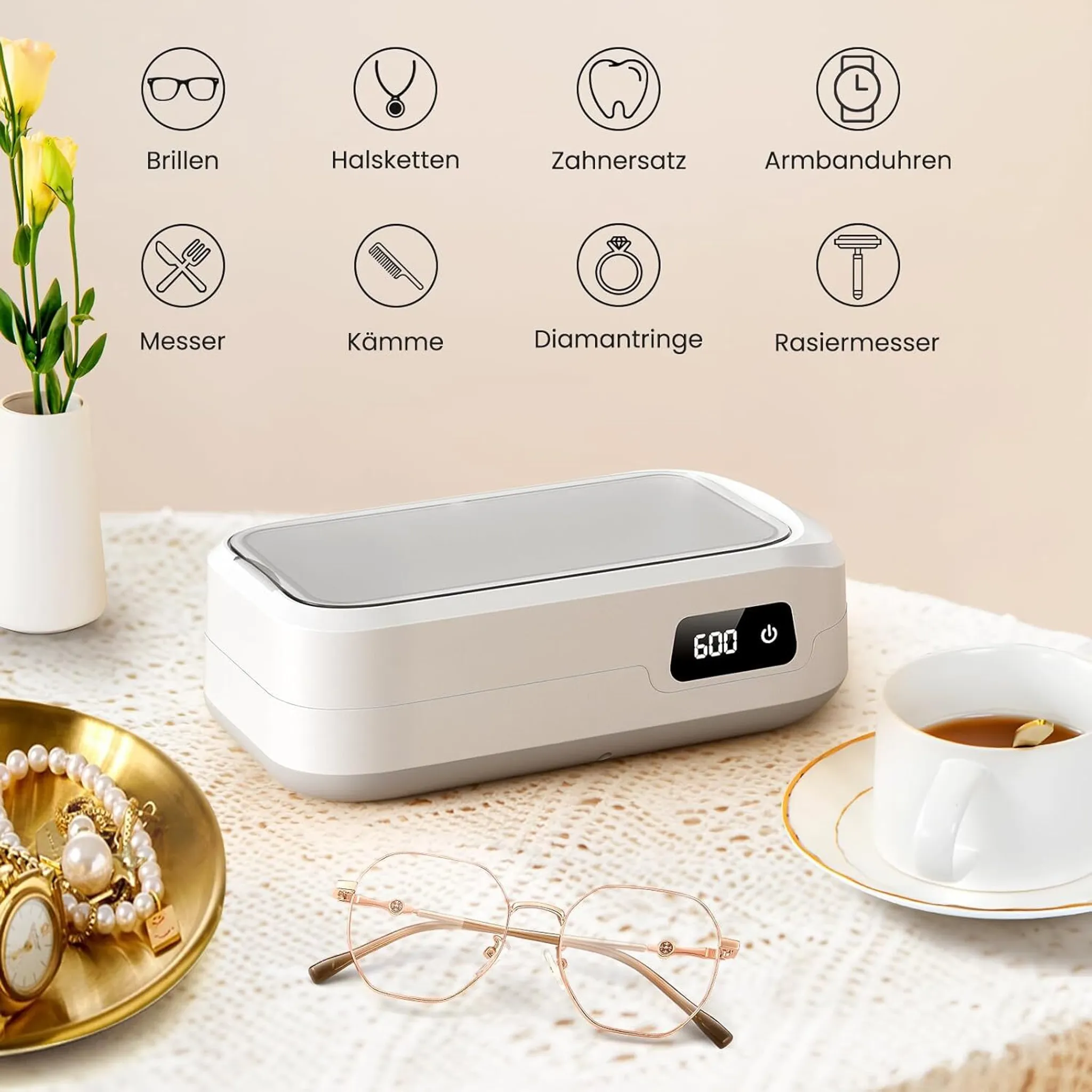 Ein weißer Ultraschallreiniger steht auf einer Tischdecke neben Schmuck, Brillen und einer Tasse Tee.