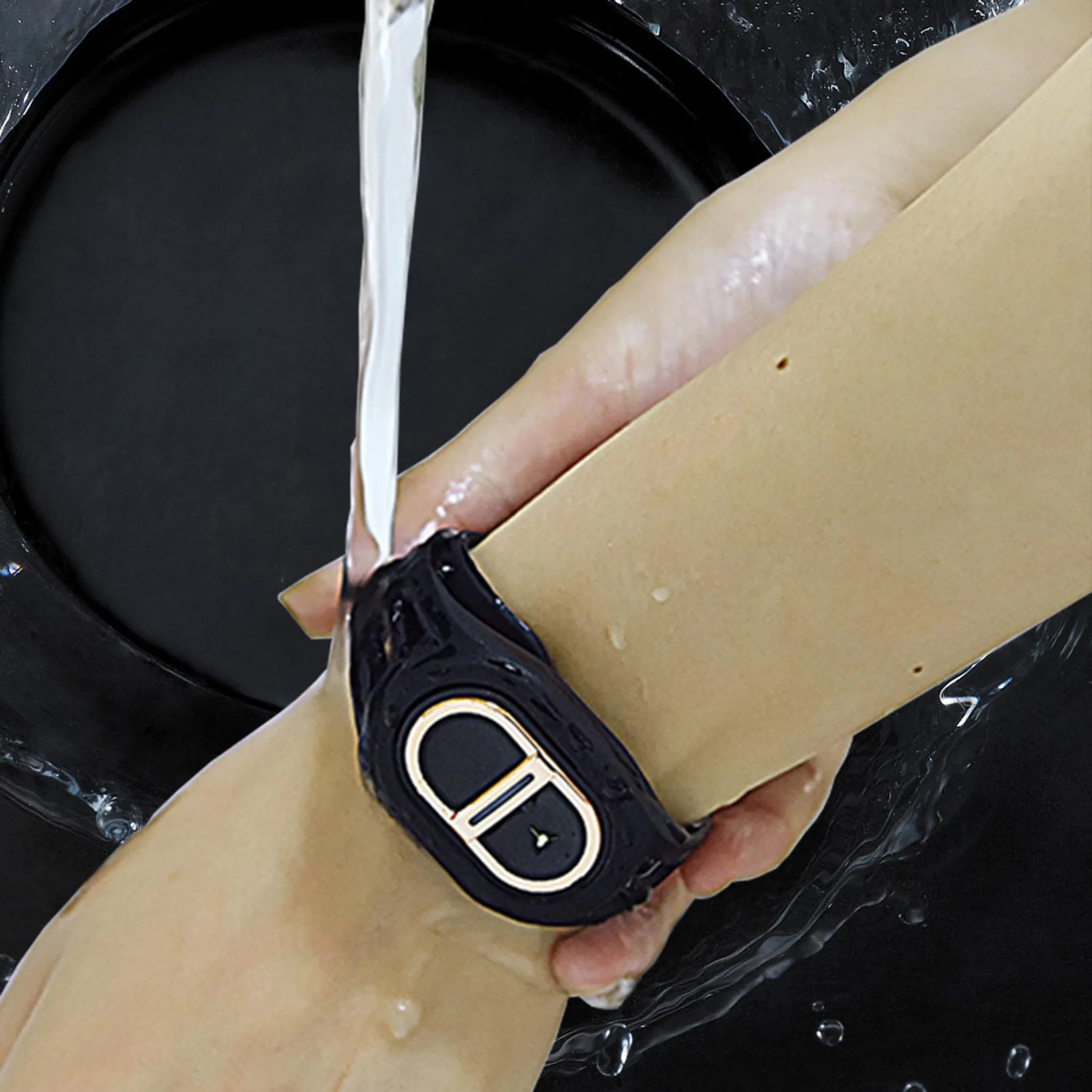Ein Arm mit einem schwarzen Armband unter fließendem Wasser.