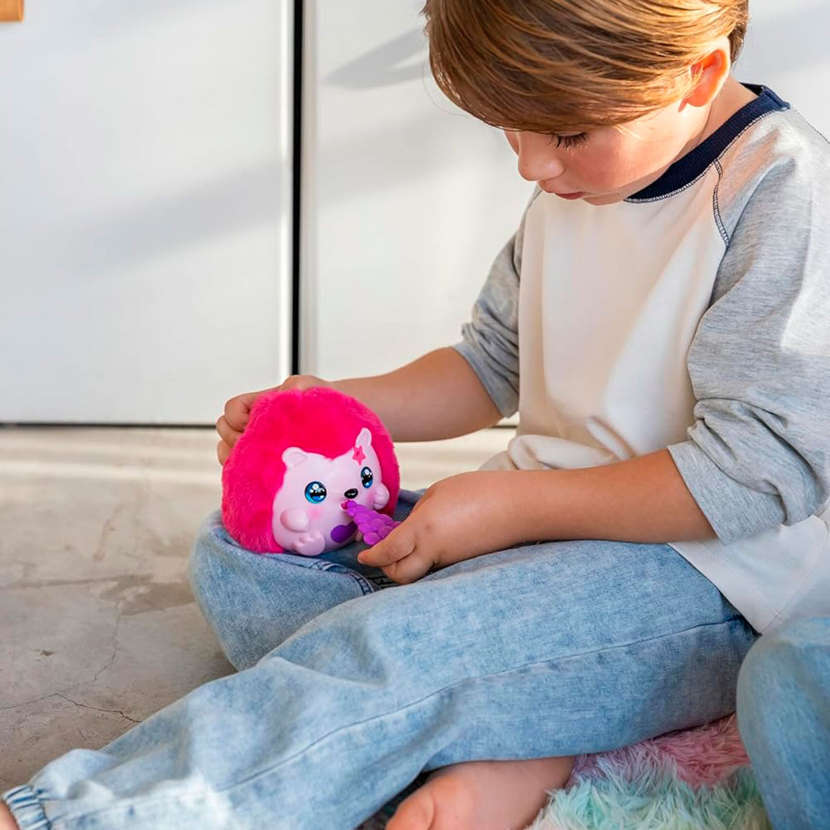 Un niño juega con un juguete de erizo rosa y esponjoso con ojos grandes.