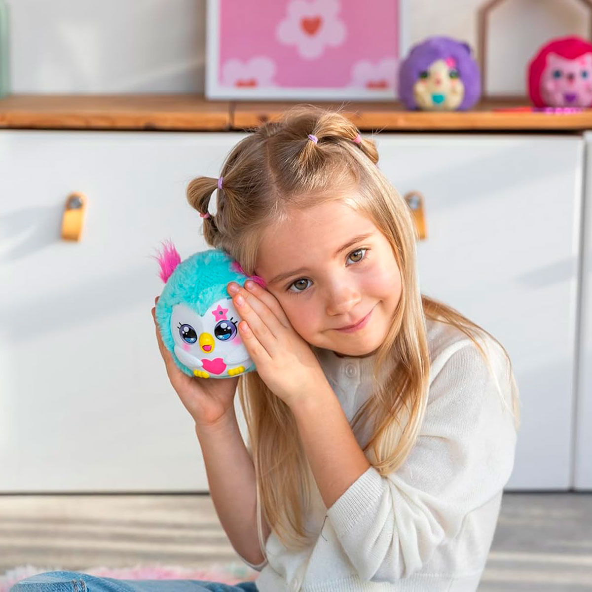 Una niña pequeña sostiene un juguete de peluche azul con orejas rosas en su oído.
