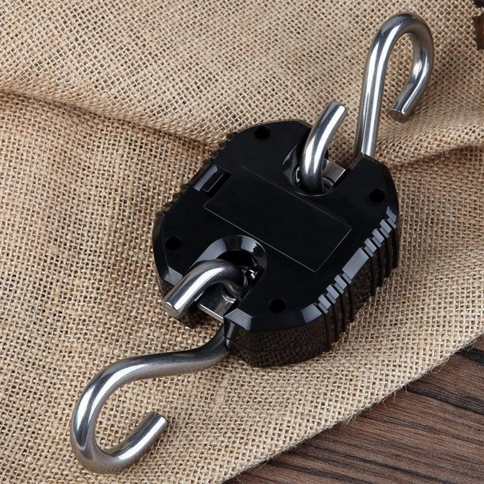 Schwarze Digitalwaage mit zwei Haken auf Jute- und Holzuntergrund.