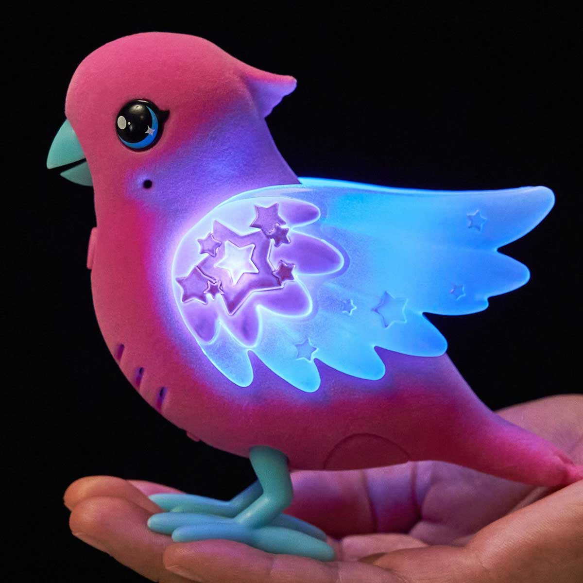 Un pájaro de juguete rosa y esponjoso con alas brillantes de estrellas se posa en una mano.