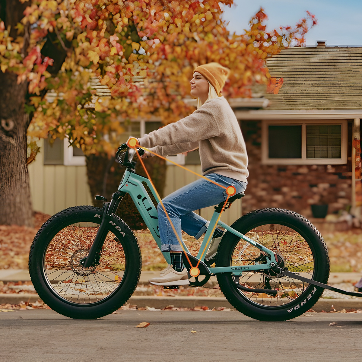 Kobieta jedzie na rowerze fatbike w kolorze teal jesienią, opadające liście.