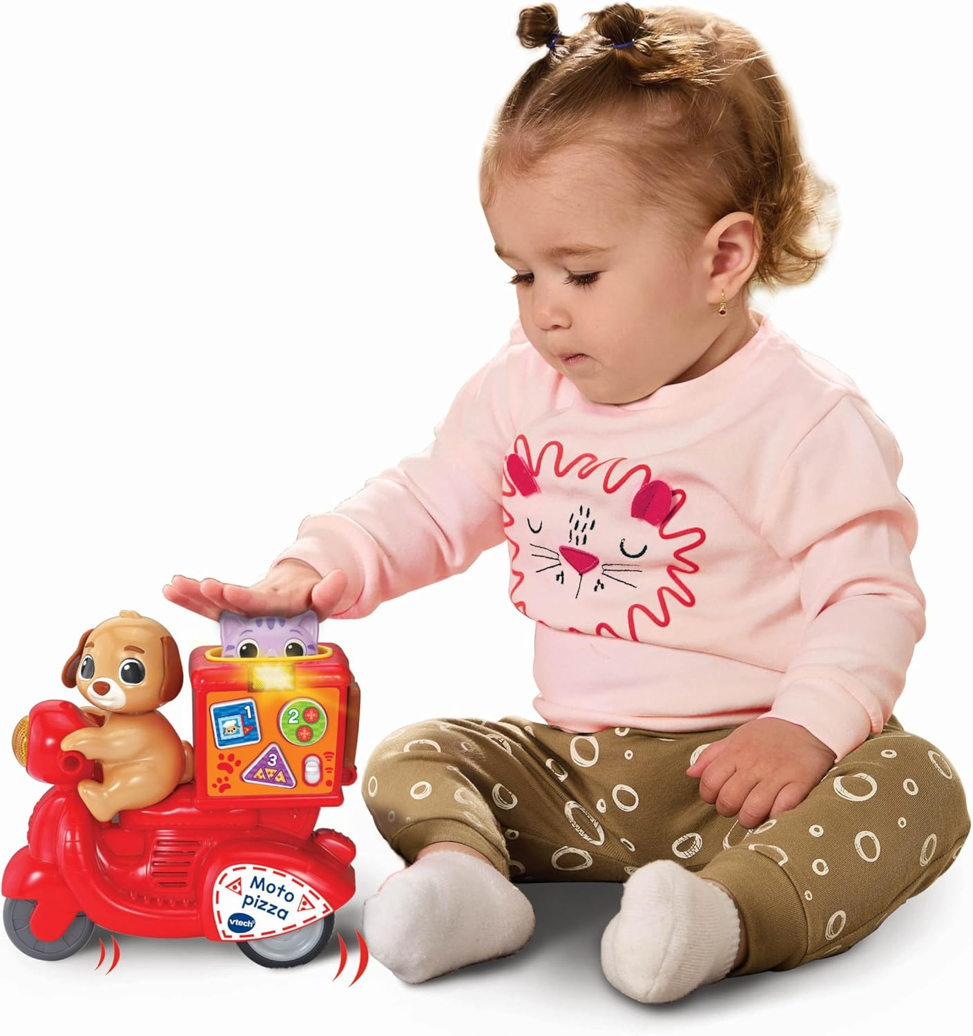 Un bebé juega con un juguete de scooter Vtech rojo con un perro y una caja de pizza.