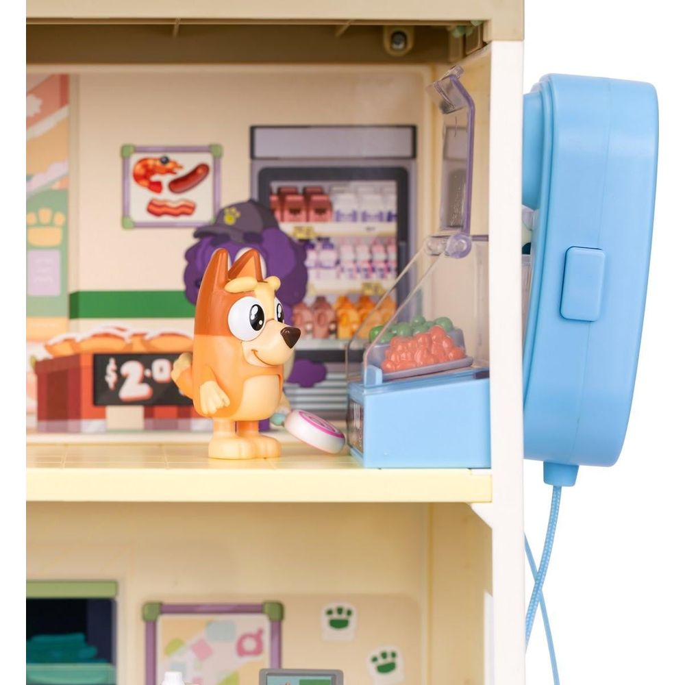 Un juguete de Bluey está en una tienda en miniatura con estantes de comida y una caja registradora azul.