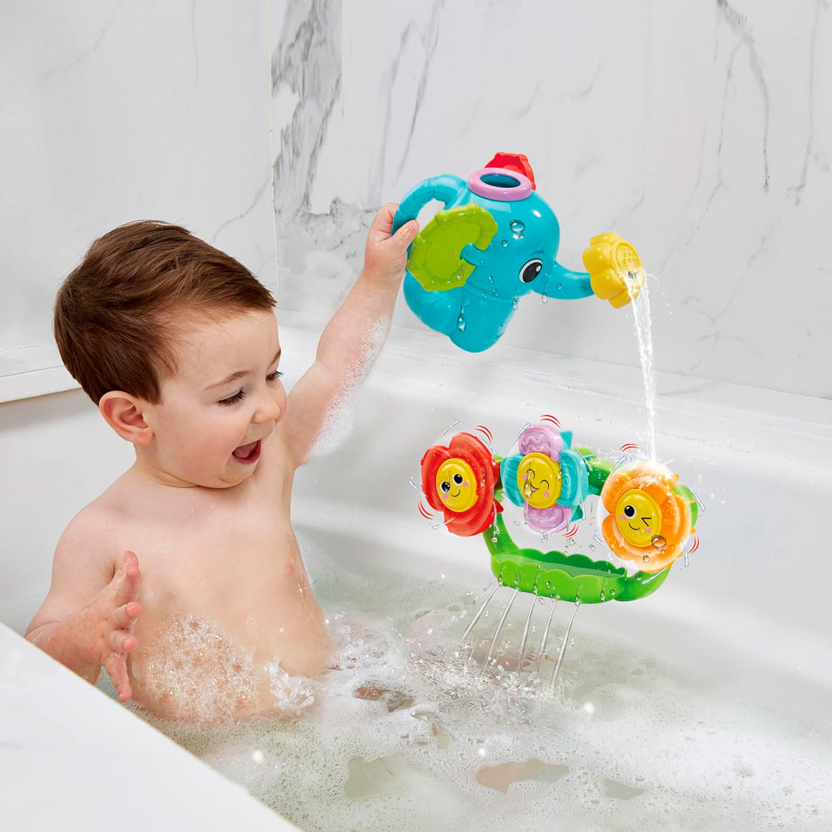 Un niño pequeño juega en la bañera con una regadera de elefante y un juguete de agua de flores.