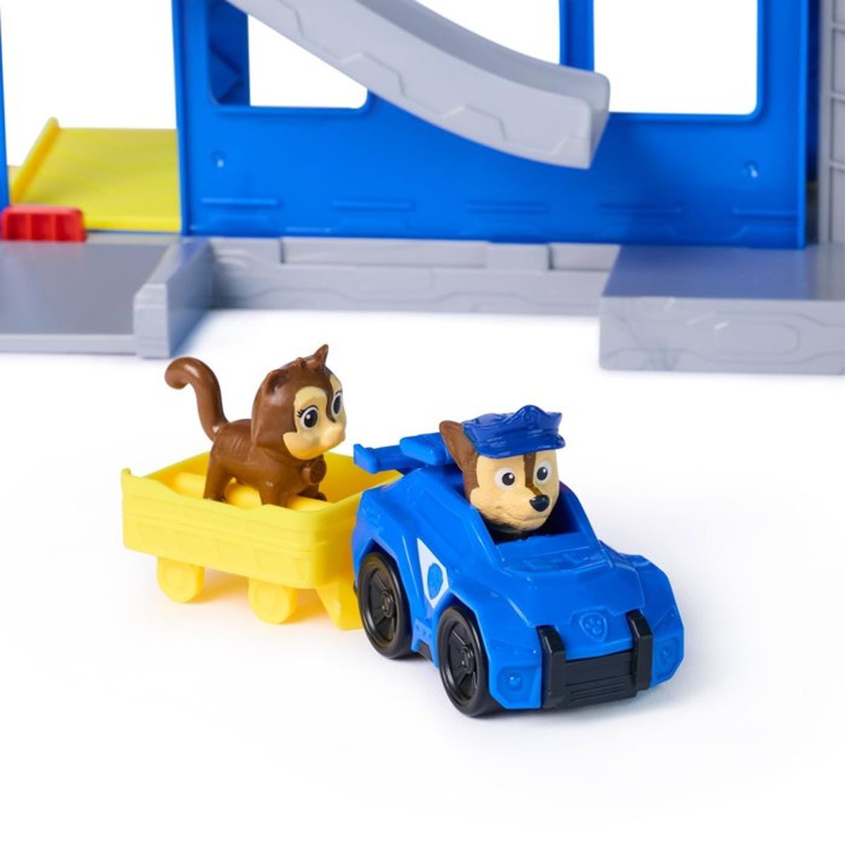 Un gato marrón en un remolque amarillo es tirado por un coche de policía azul con Chase.