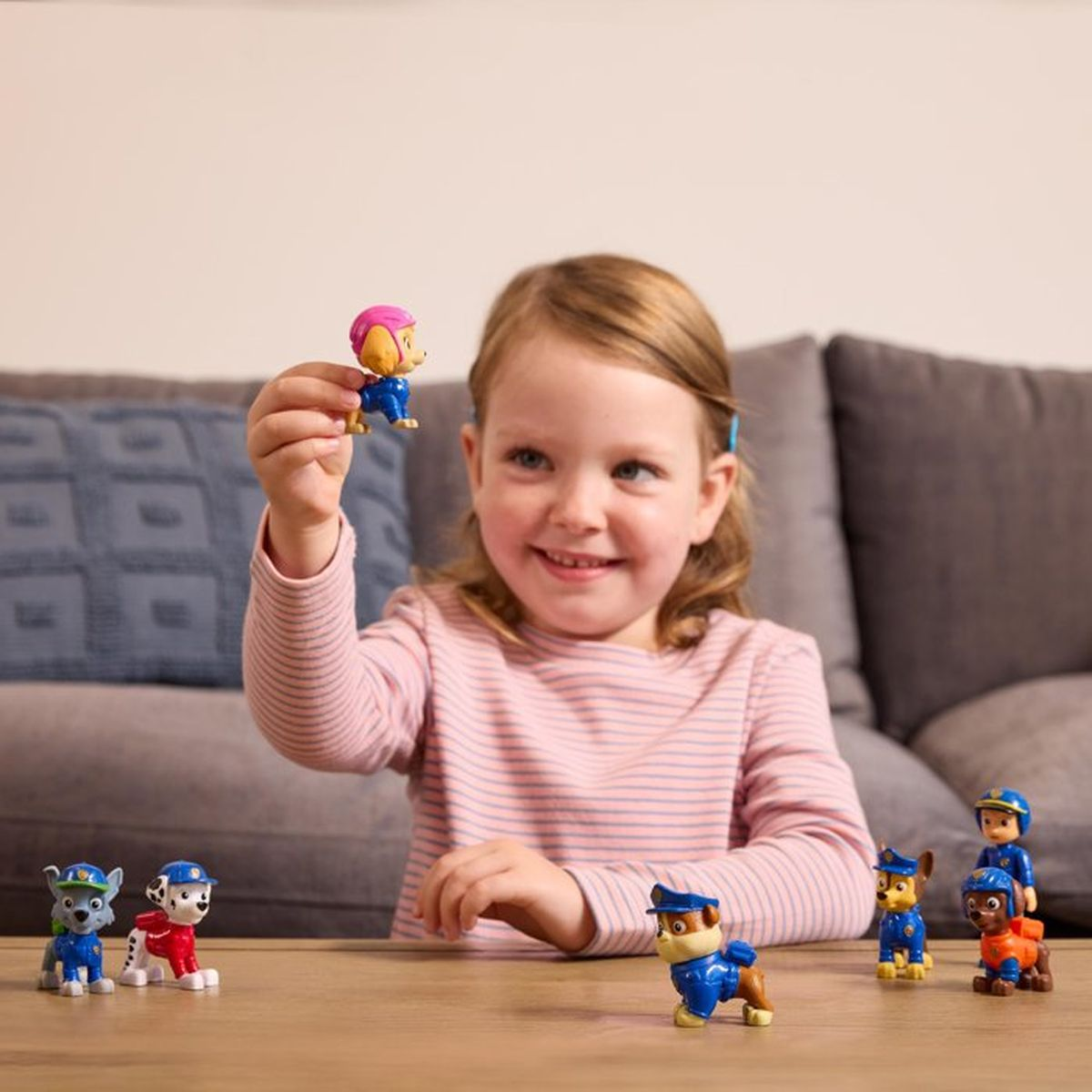 Una niña levanta una figura de Skye mientras otras figuras de Paw Patrol están sobre una mesa.