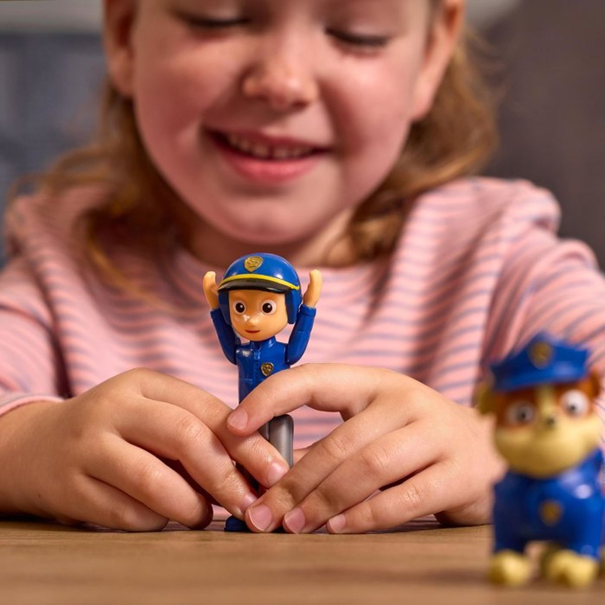 Una niña juega con figuras de Paw Patrol sobre una mesa de madera.