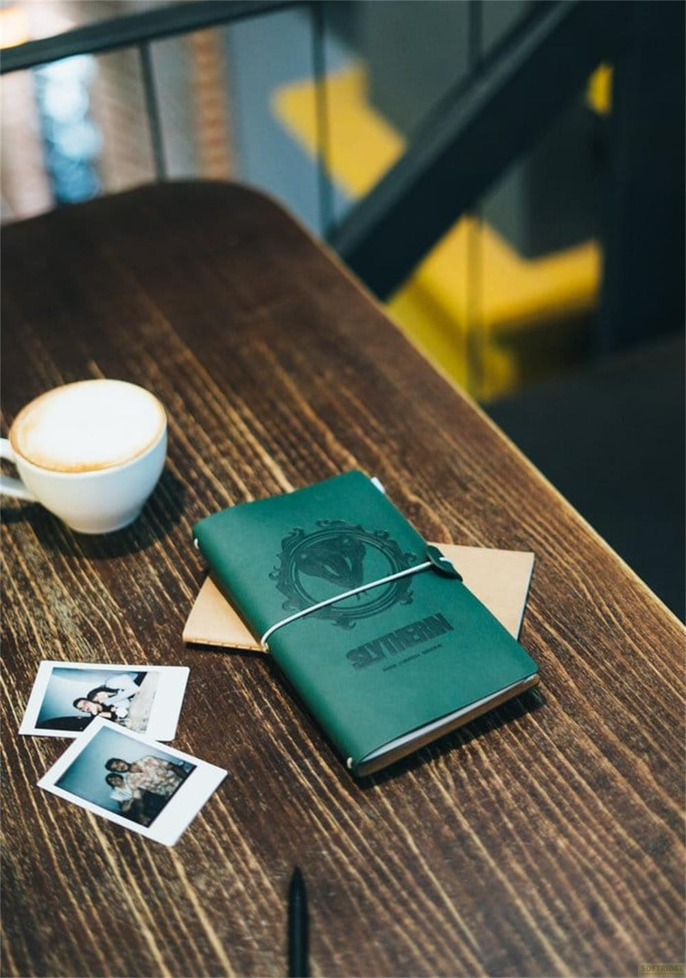 Un cuaderno verde de Slytherin, café y dos fotos sobre una mesa de madera.