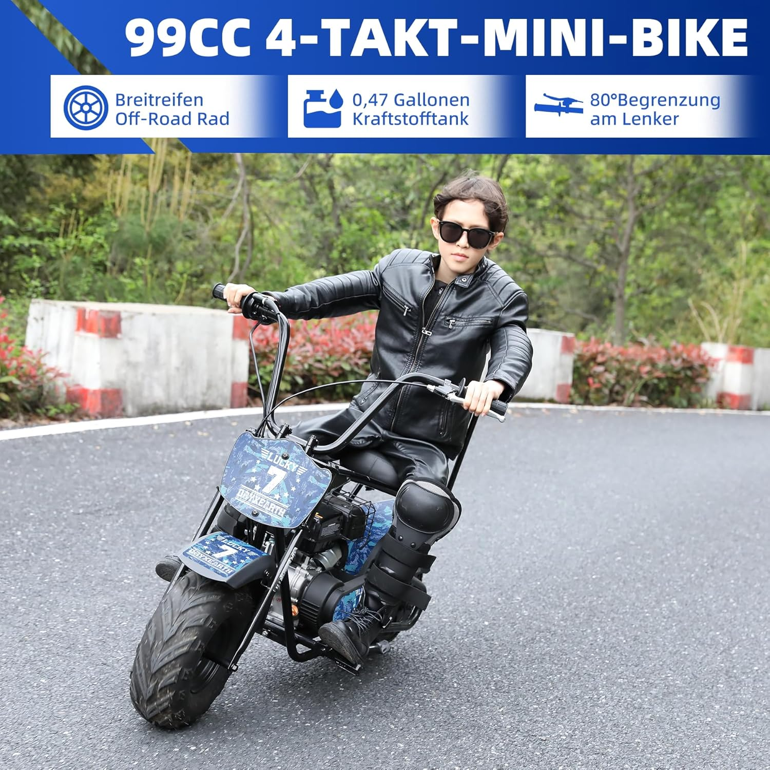 Ein Junge in Lederkleidung fährt ein Mini-Bike auf einer asphaltierten Straße, mit Bäumen im Hintergrund.