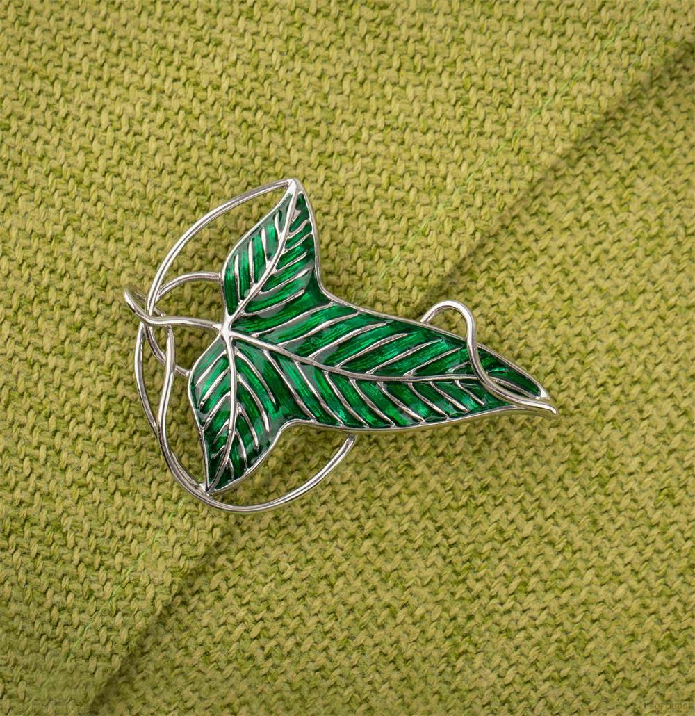 Une broche argentée en forme de feuille verte aux nervures argentées, sur un tissu tricoté vert.