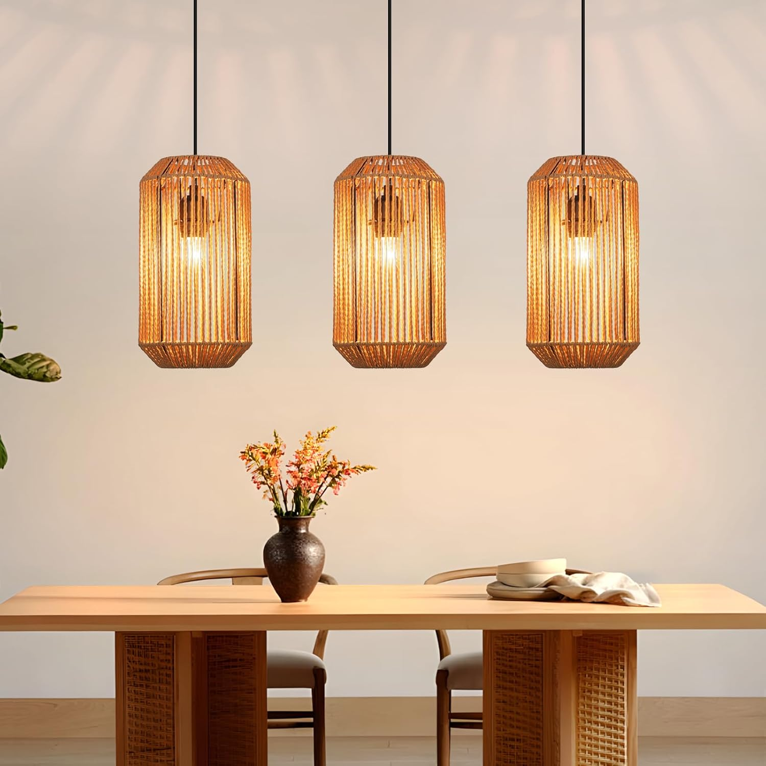 Tre lampade a sospensione in rattan sopra un tavolo di legno con vaso e fiori.