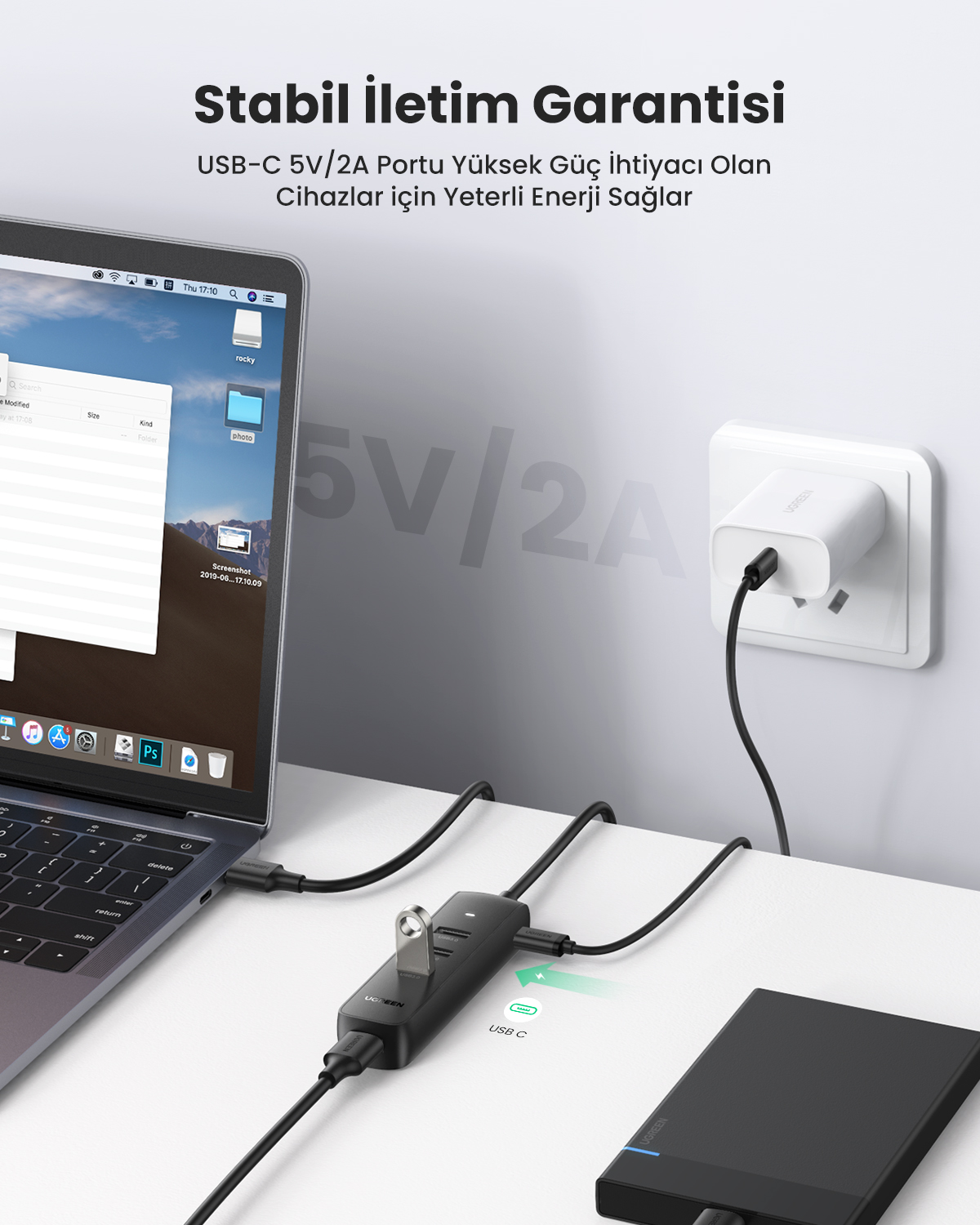 Laptop jest podłączony do czarnego huba USB-C zasilającego zewnętrzny dysk twardy i zasilacz sieciowy.