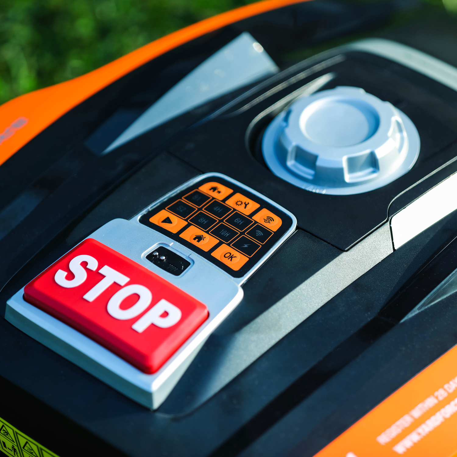 Bedienfeld eines Mähroboters mit rotem STOP-Knopf und orangen Tasten.