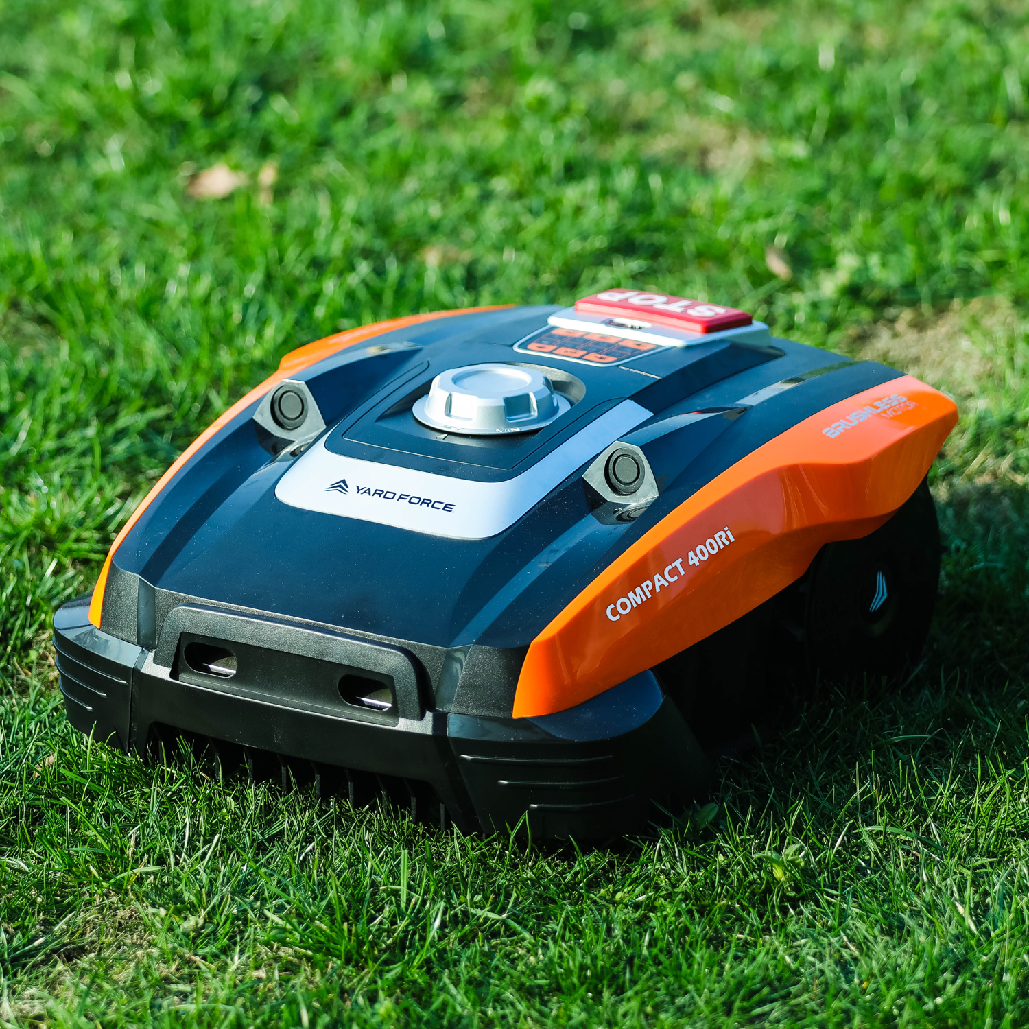 Ein schwarzer und oranger Rasenmähroboter steht auf einem grünen Rasen.