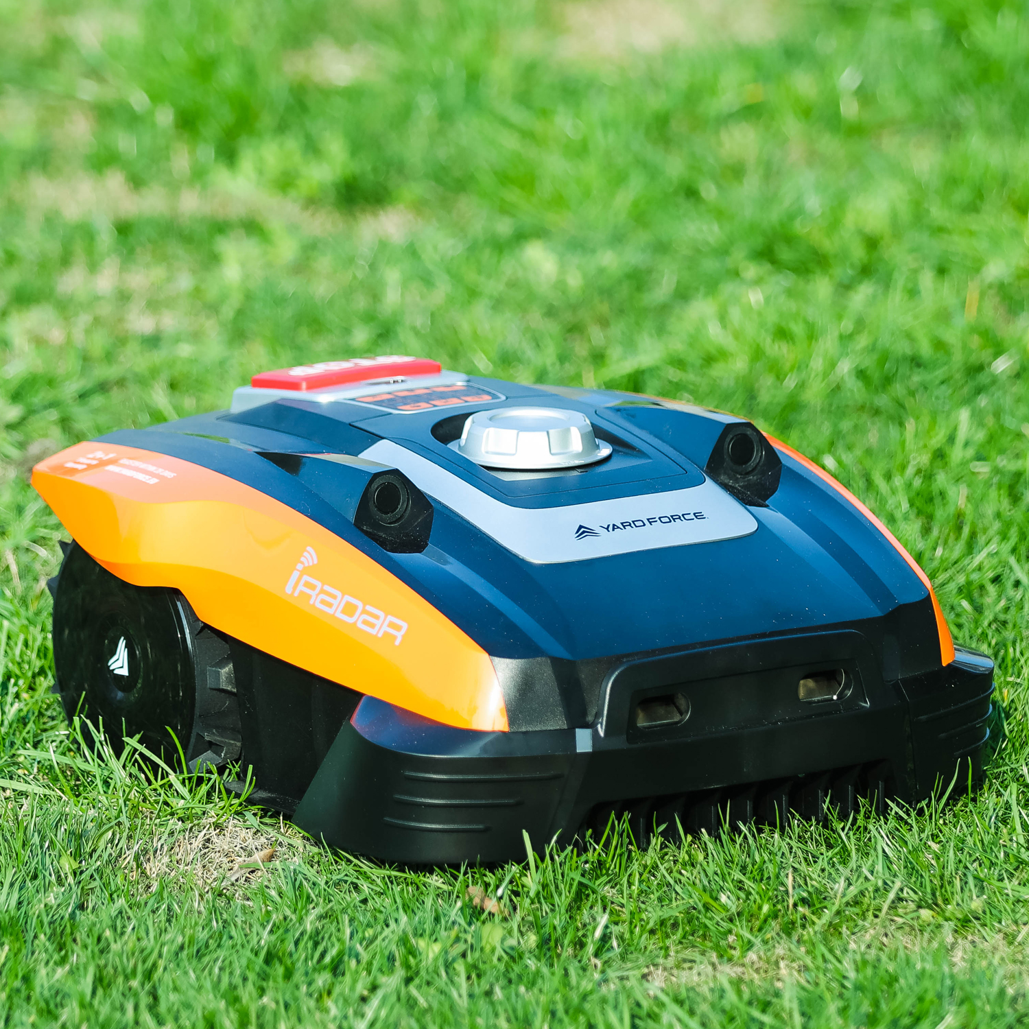 Ein orangefarbener und schwarzer Mähroboter steht auf einem grünen Rasen.