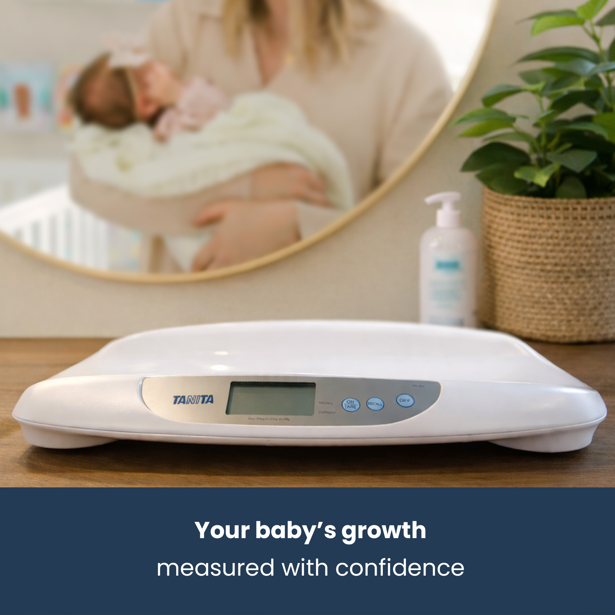 A white baby scale with a display sits on a wooden table. A person holds a baby.