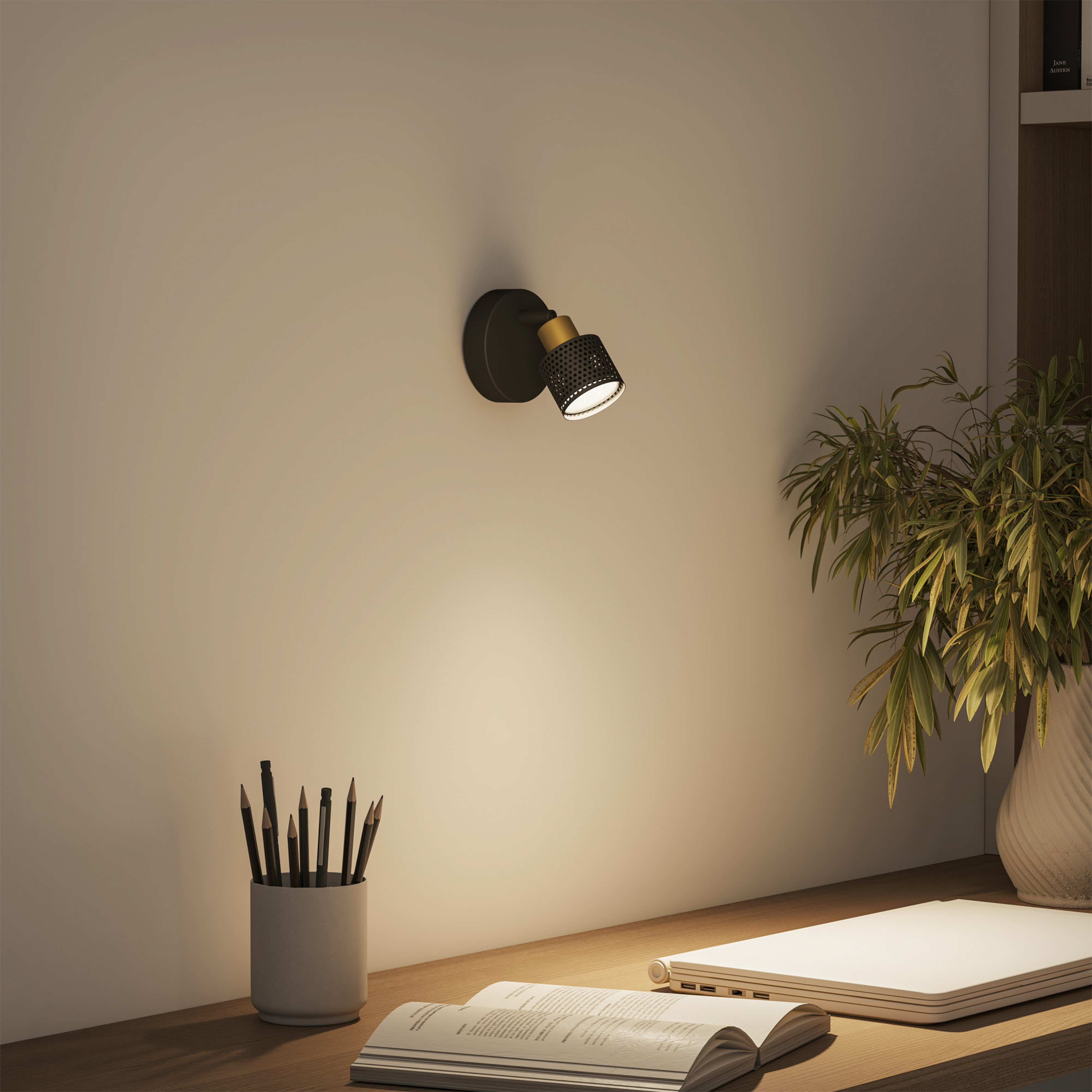 Ein schwarzer Wandspot mit goldenen Akzenten beleuchtet einen Schreibtisch mit Büchern und Stiften.