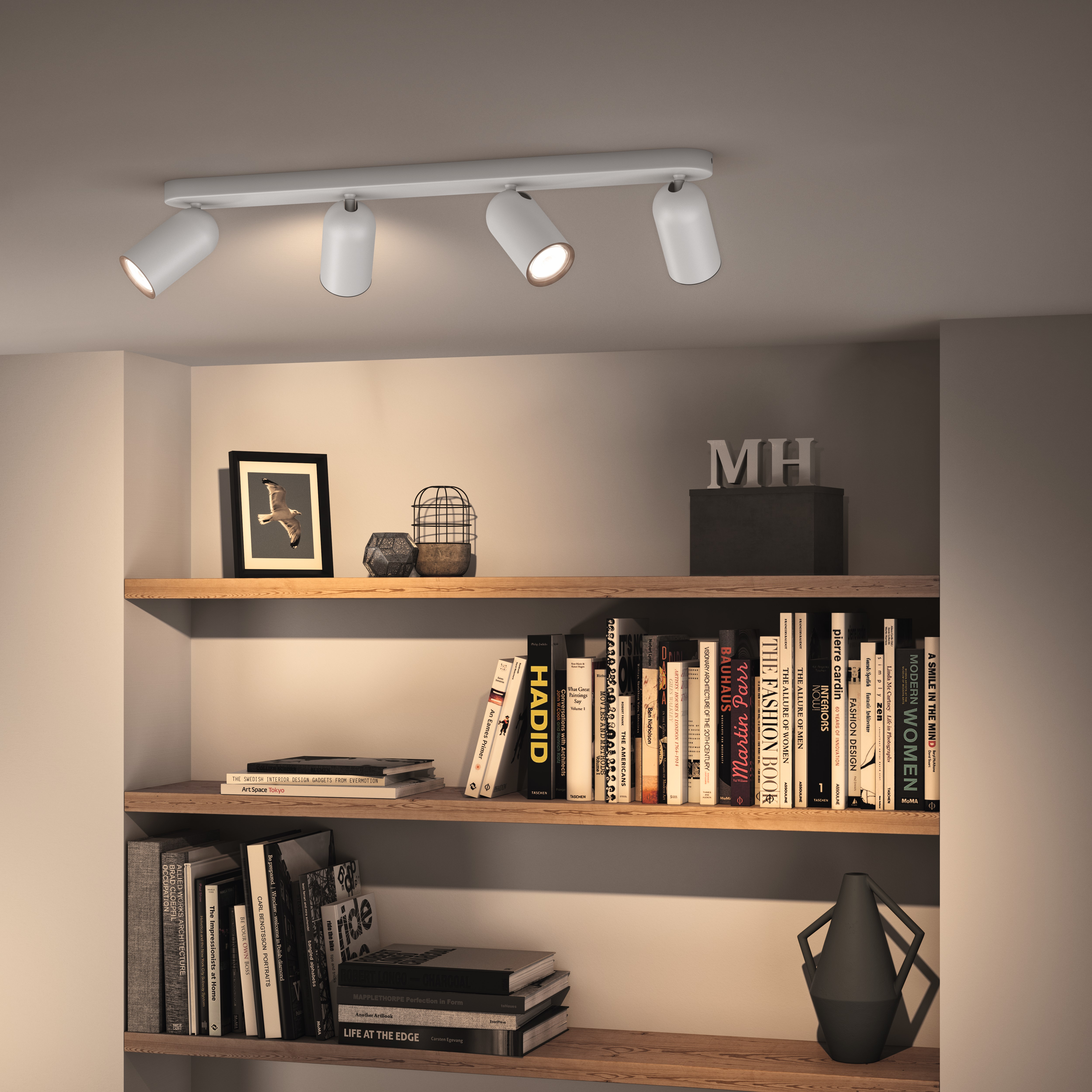 Ein weißer Deckenstrahler beleuchtet ein Bücherregal mit Büchern und Dekoration.
