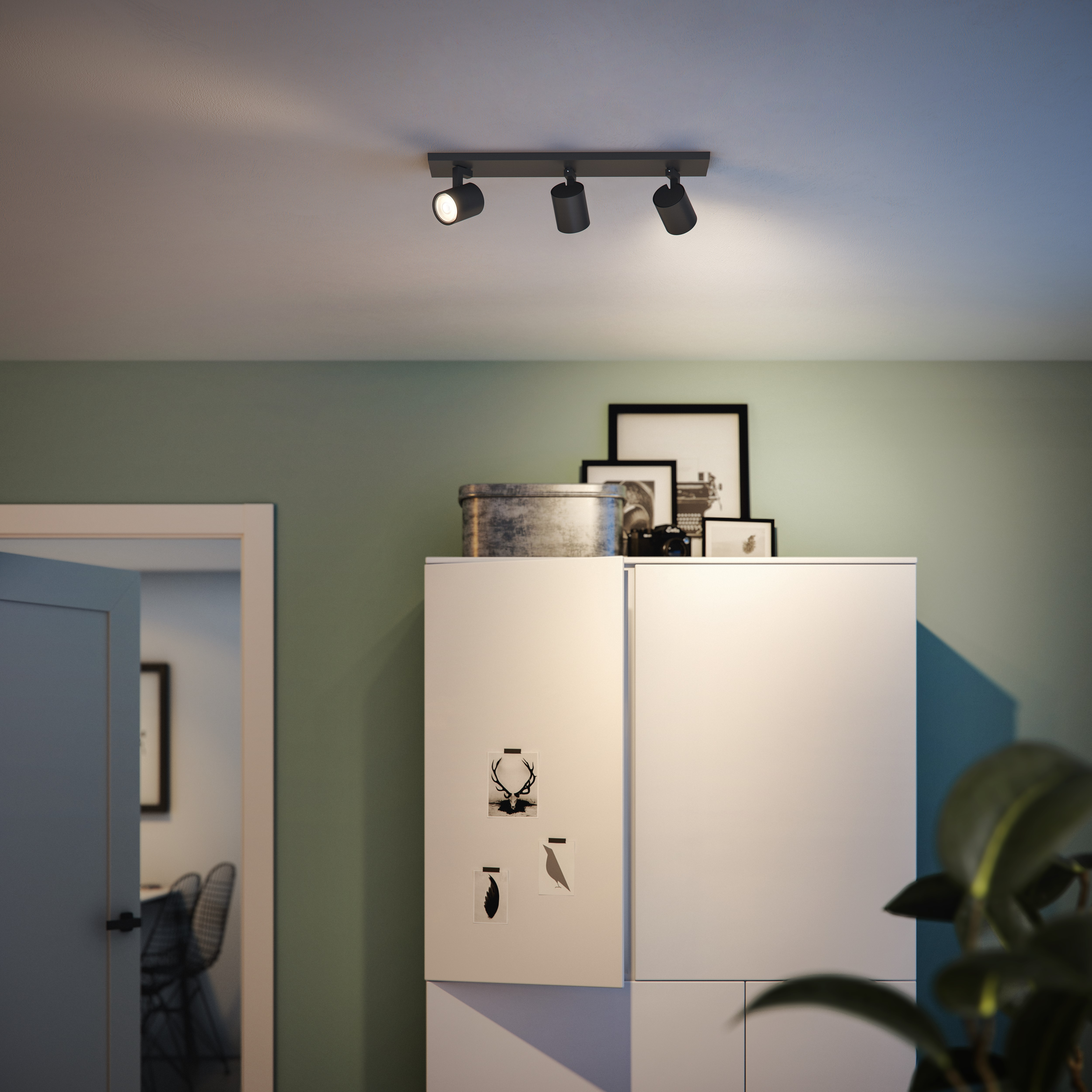 Schwarze Deckenleuchte mit drei Spots über einem weißen Schrank.