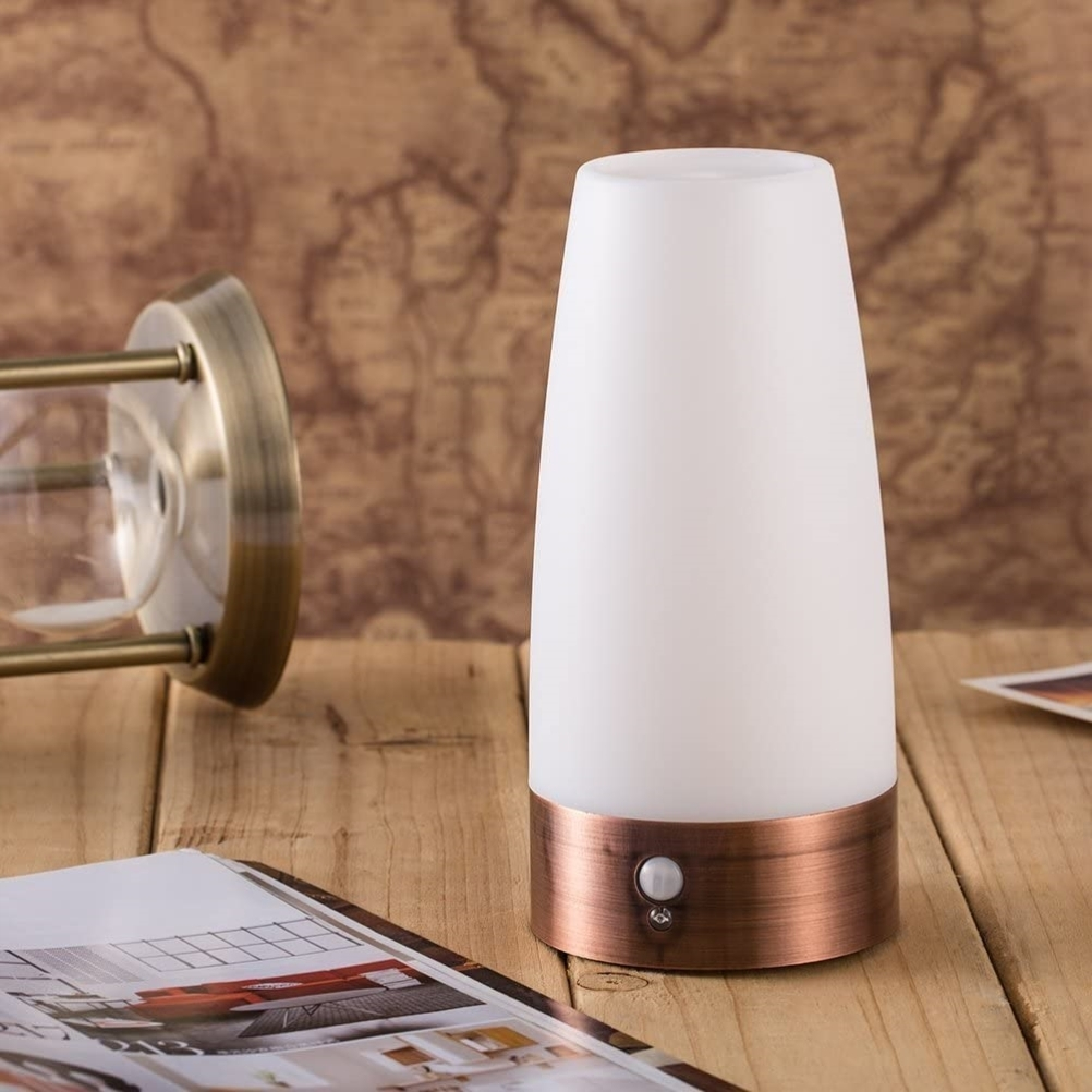 Eine weiße Lampe mit Kupfersockel steht auf einem Holztisch neben einem Buch.