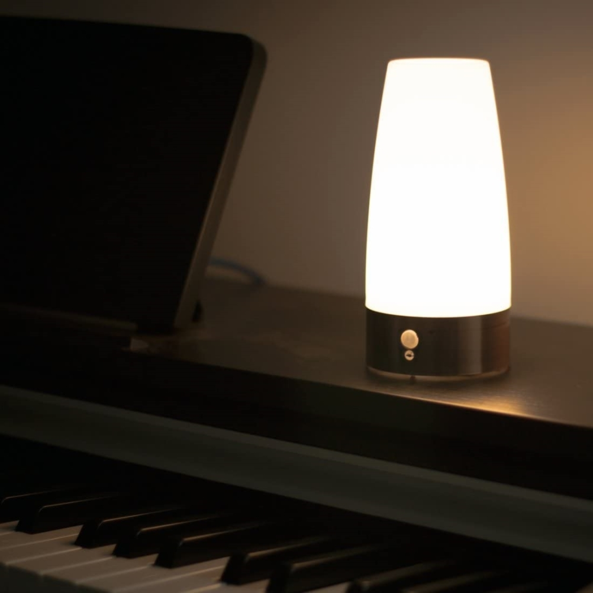 Eine weiße Lampe steht auf einem Klavier neben einem dunklen Bildschirm.