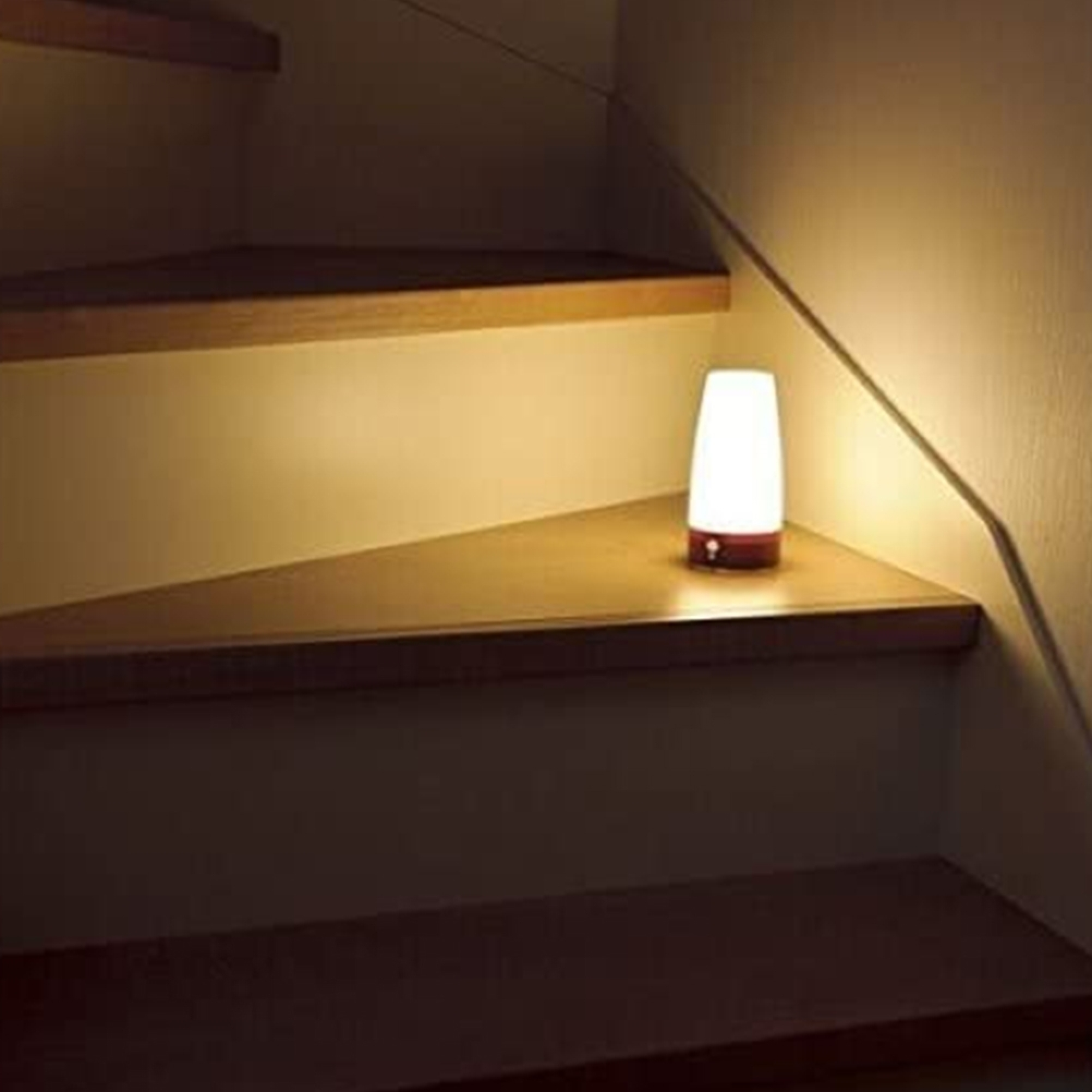 Eine weiße Lampe mit rotem Sockel steht auf einer Holztreppe.