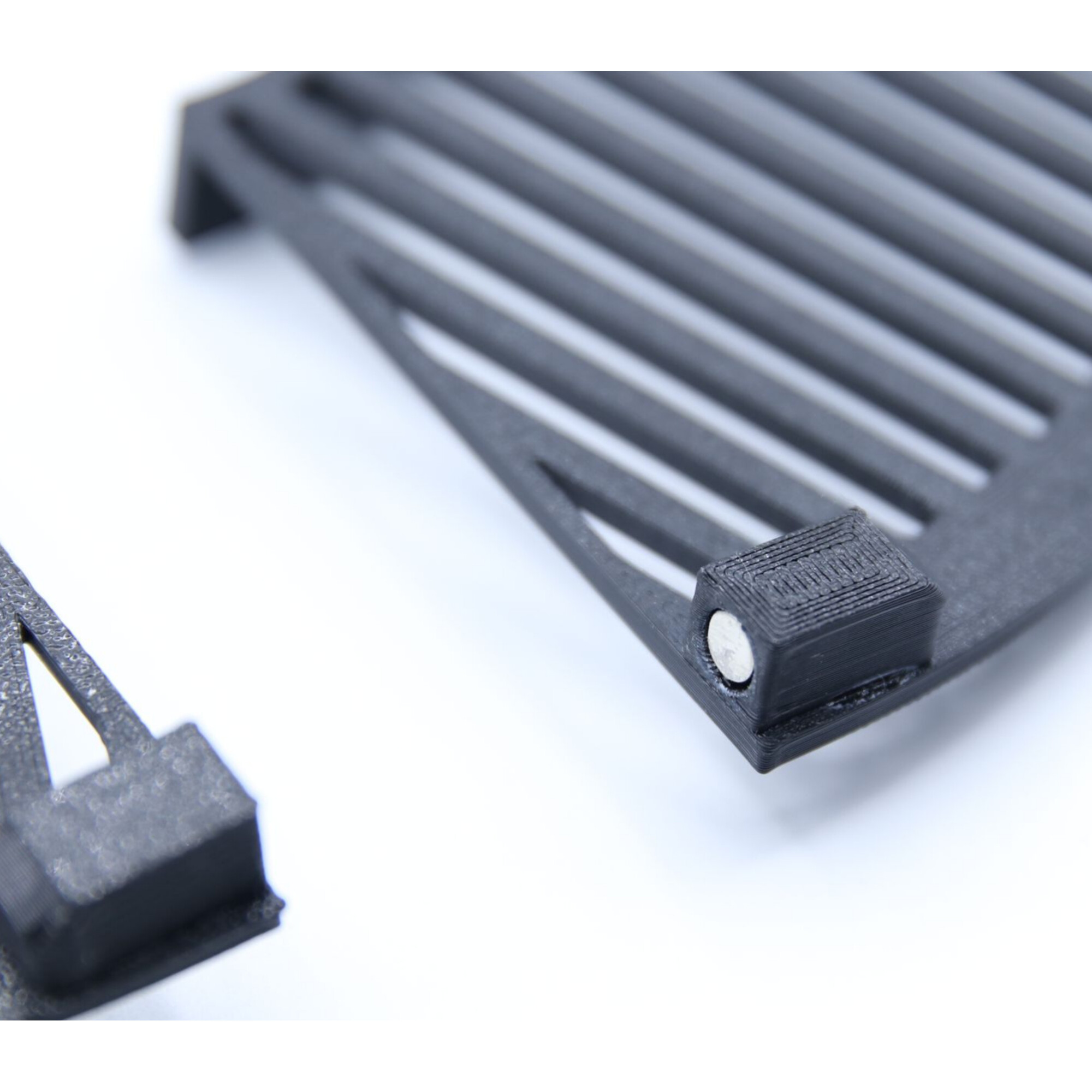 Schwarzes 3D-gedrucktes Teil mit Rillen und einem kleinen silbernen Zylinder.