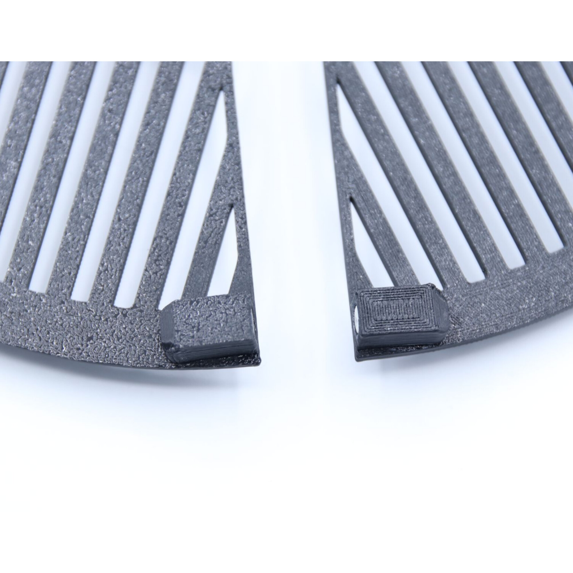 Zwei graue, ventilationsartige Teile mit weißen Streifen und schwarzen 3D-gedruckten Elementen.