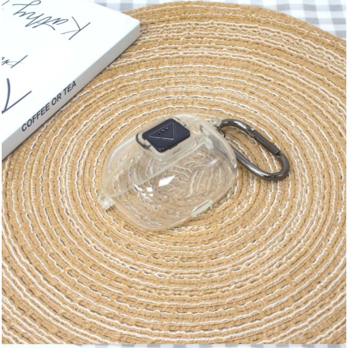 Transparente Hülle mit silbernem Karabiner auf einem runden, geflochtenen Untersetzer.