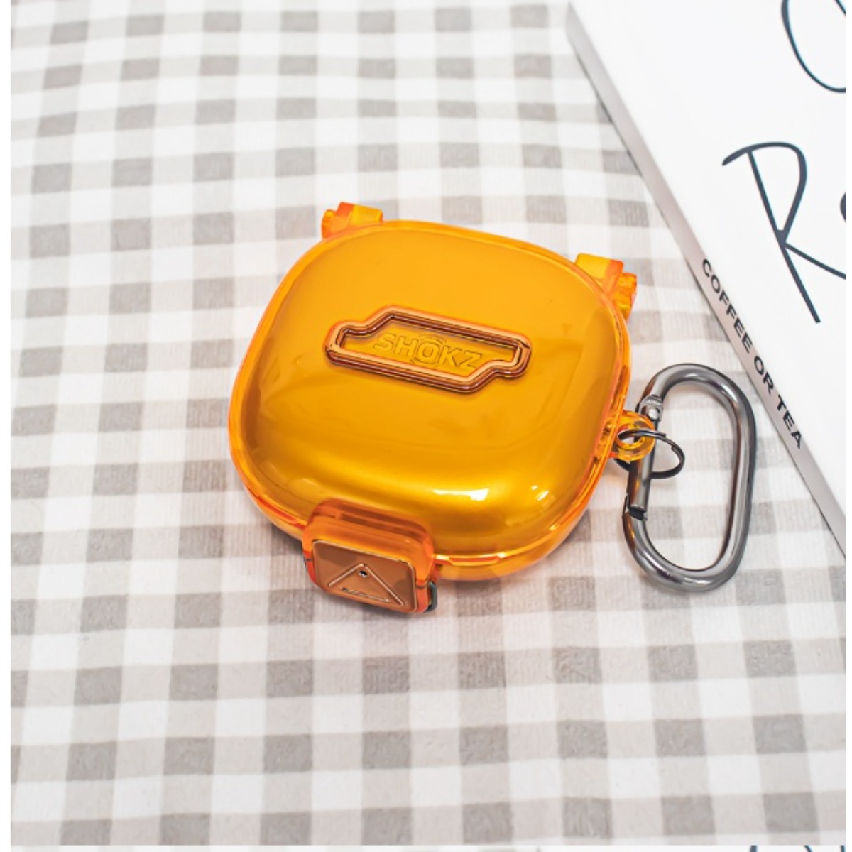 Orange Shokz Hülle mit silbernem Karabiner auf kariertem Hintergrund.
