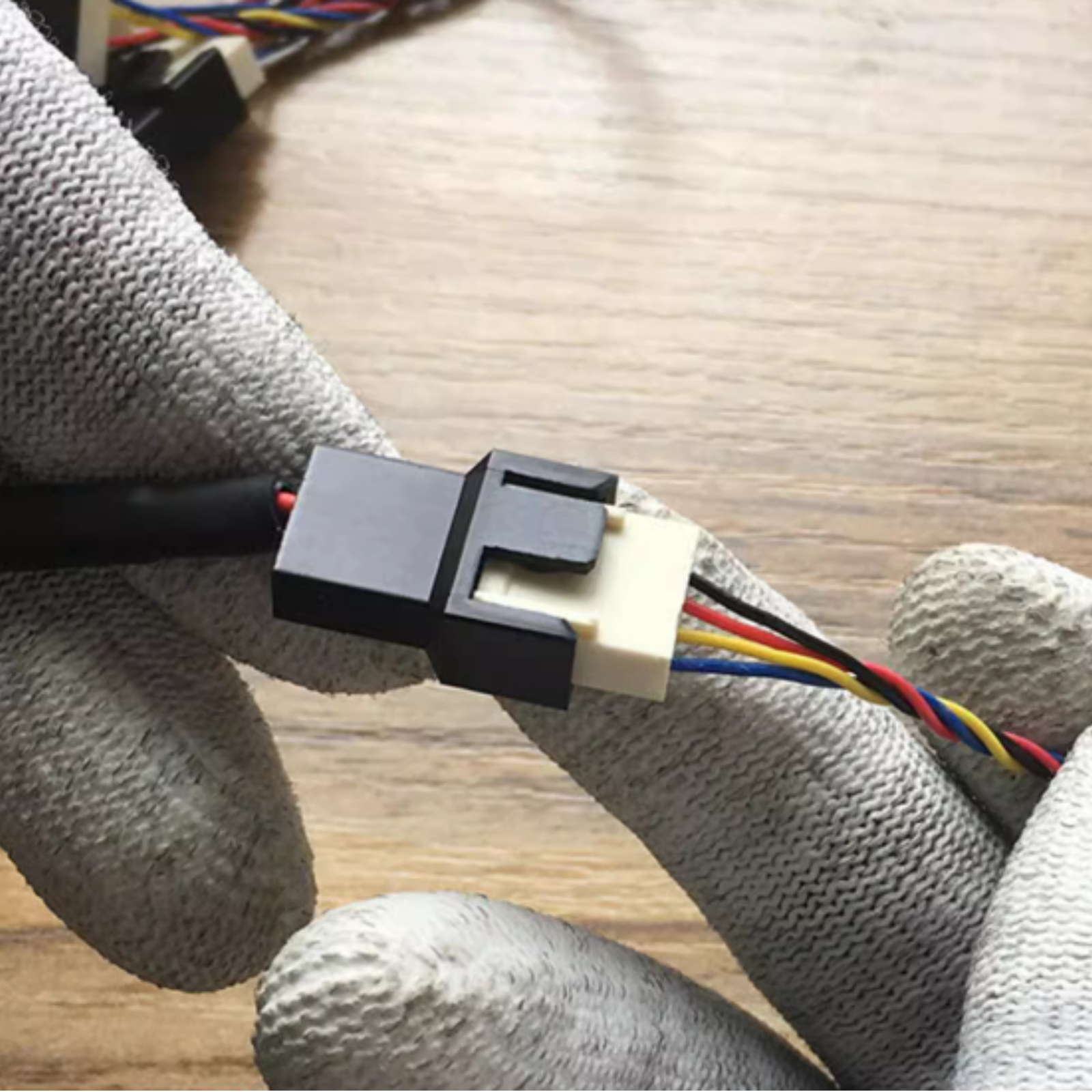 Hände in grauen Handschuhen verbinden ein schwarzes Kabel mit einem weißen Stecker mit bunten Drähten.
