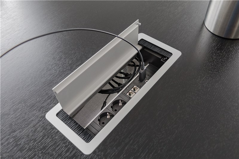 Ein Tischanschlussfeld mit Steckdosen, USB und Netzwerkanschlüssen auf einem dunklen Holztisch.