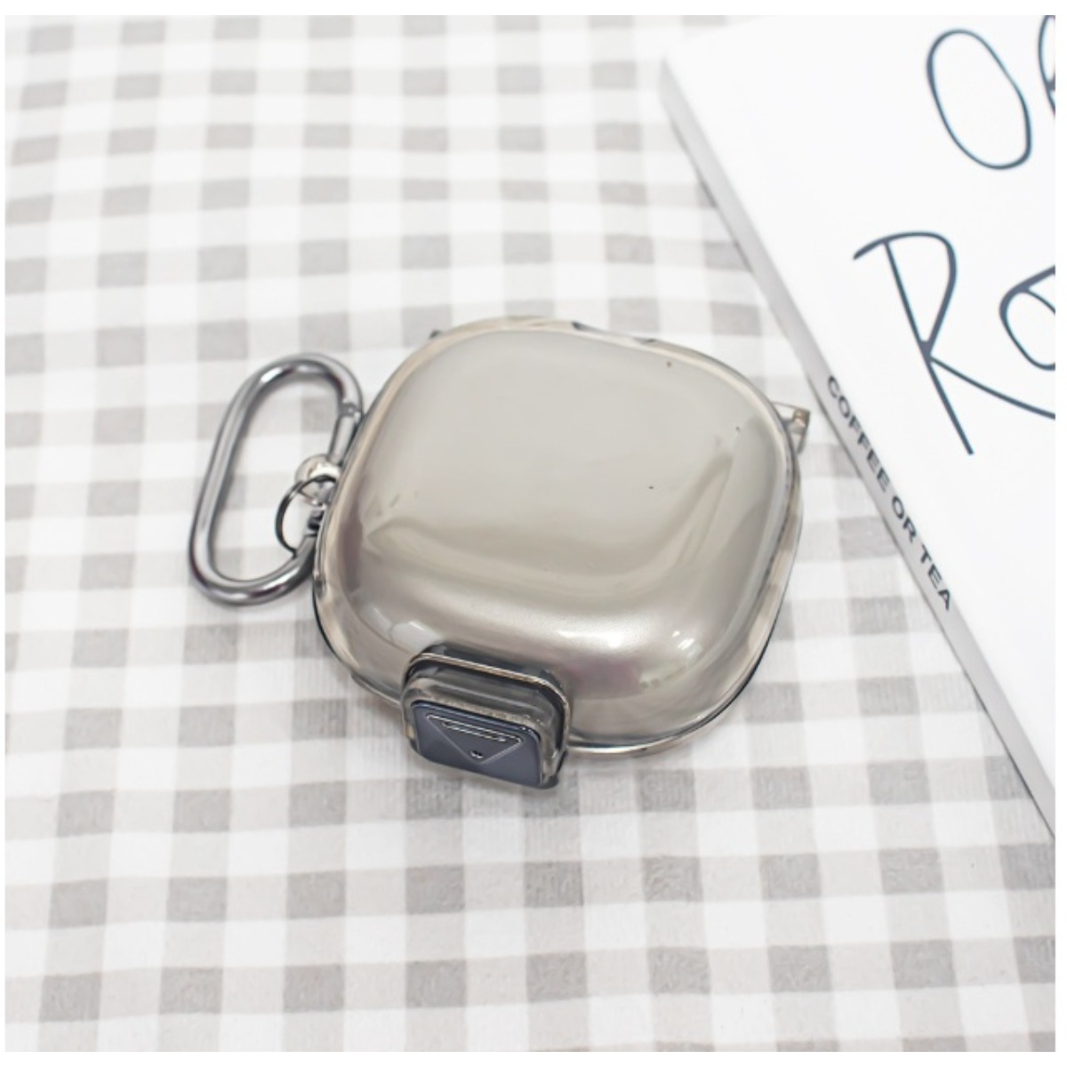Ein glänzendes silbernes Etui mit einem Karabinerhaken und einem Buch daneben.