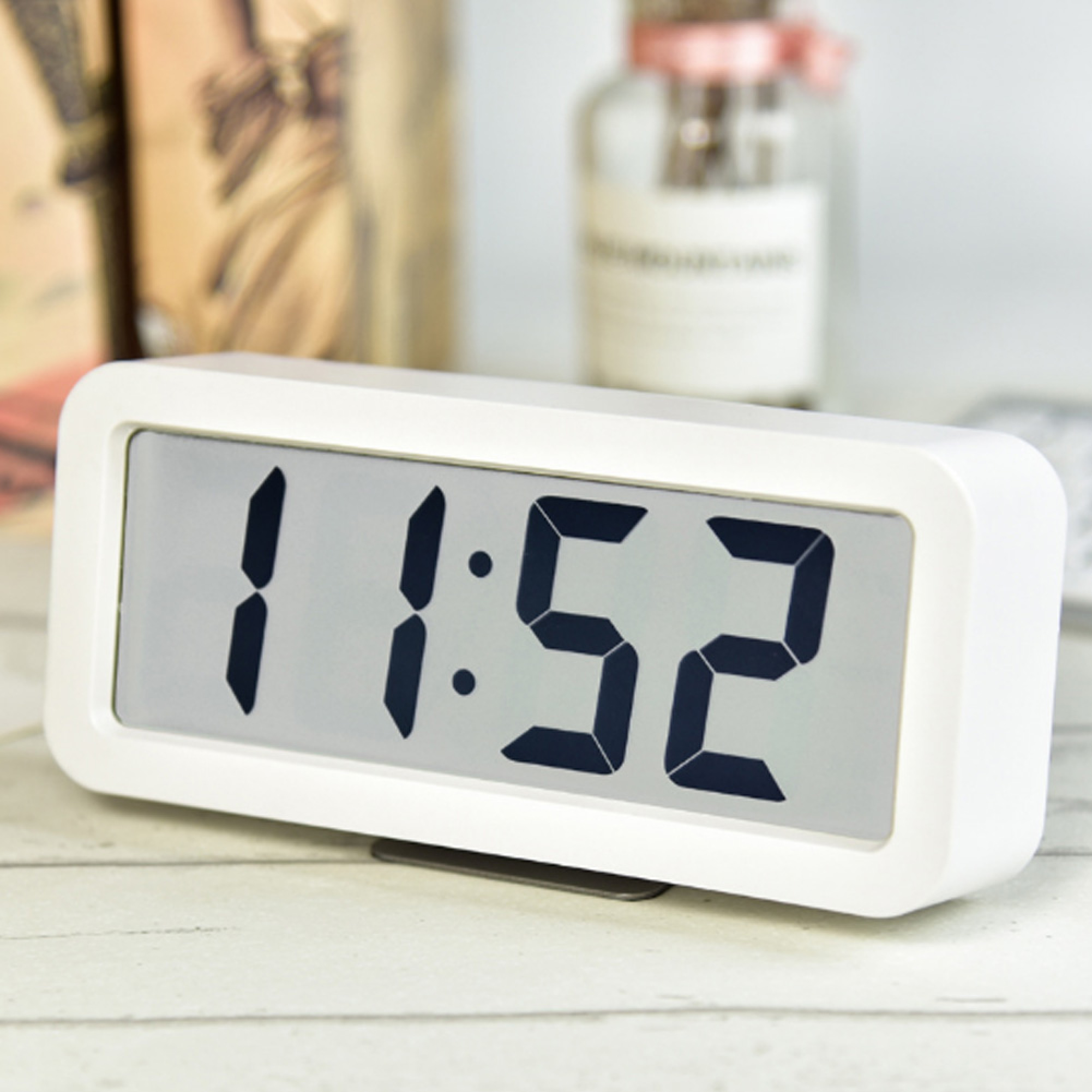 Ein weißer Digitalwecker zeigt 11:52 an, steht auf einem Holztisch.