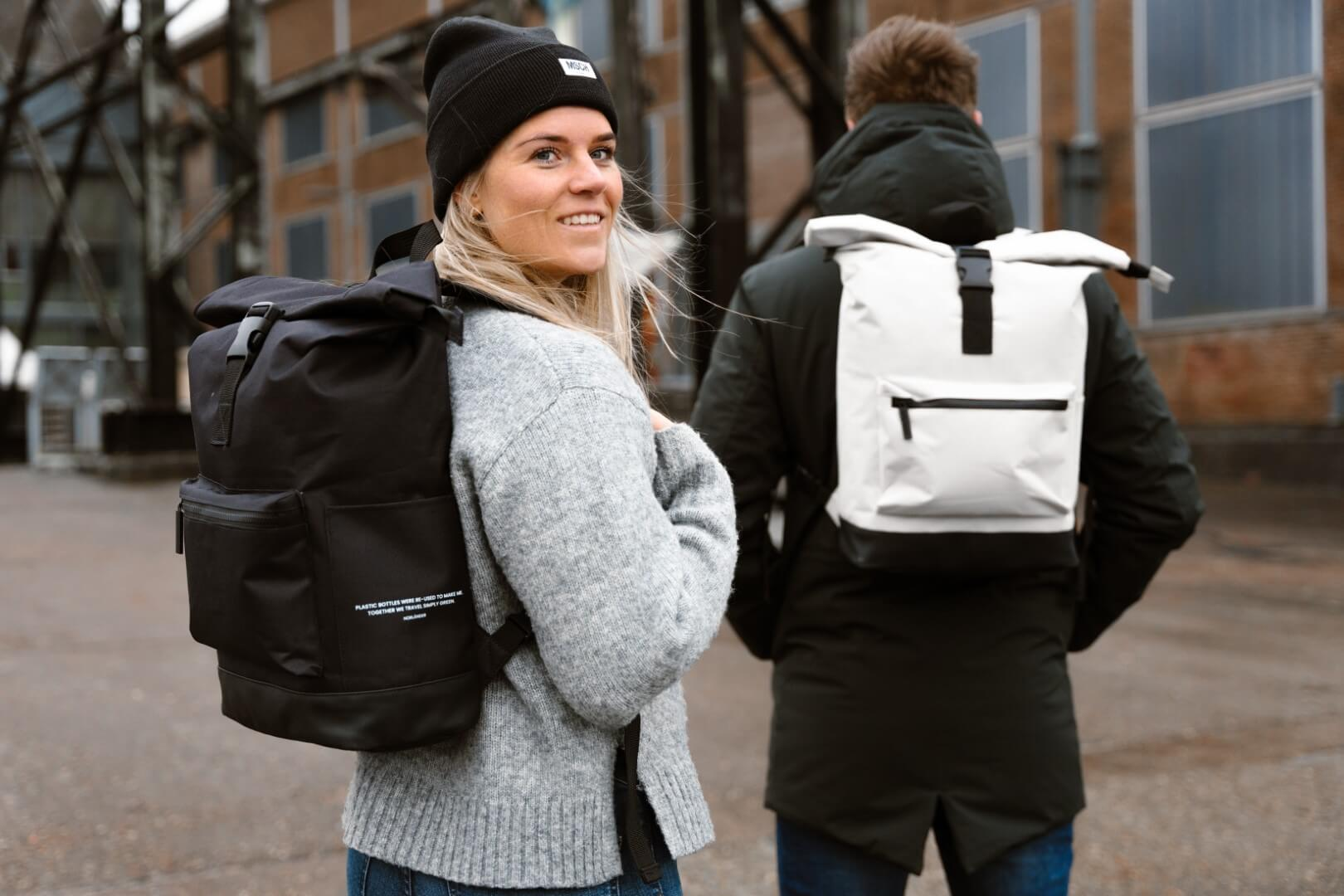 Eine Frau mit schwarzer Mütze und ein Mann mit Rucksack stehen draußen.
